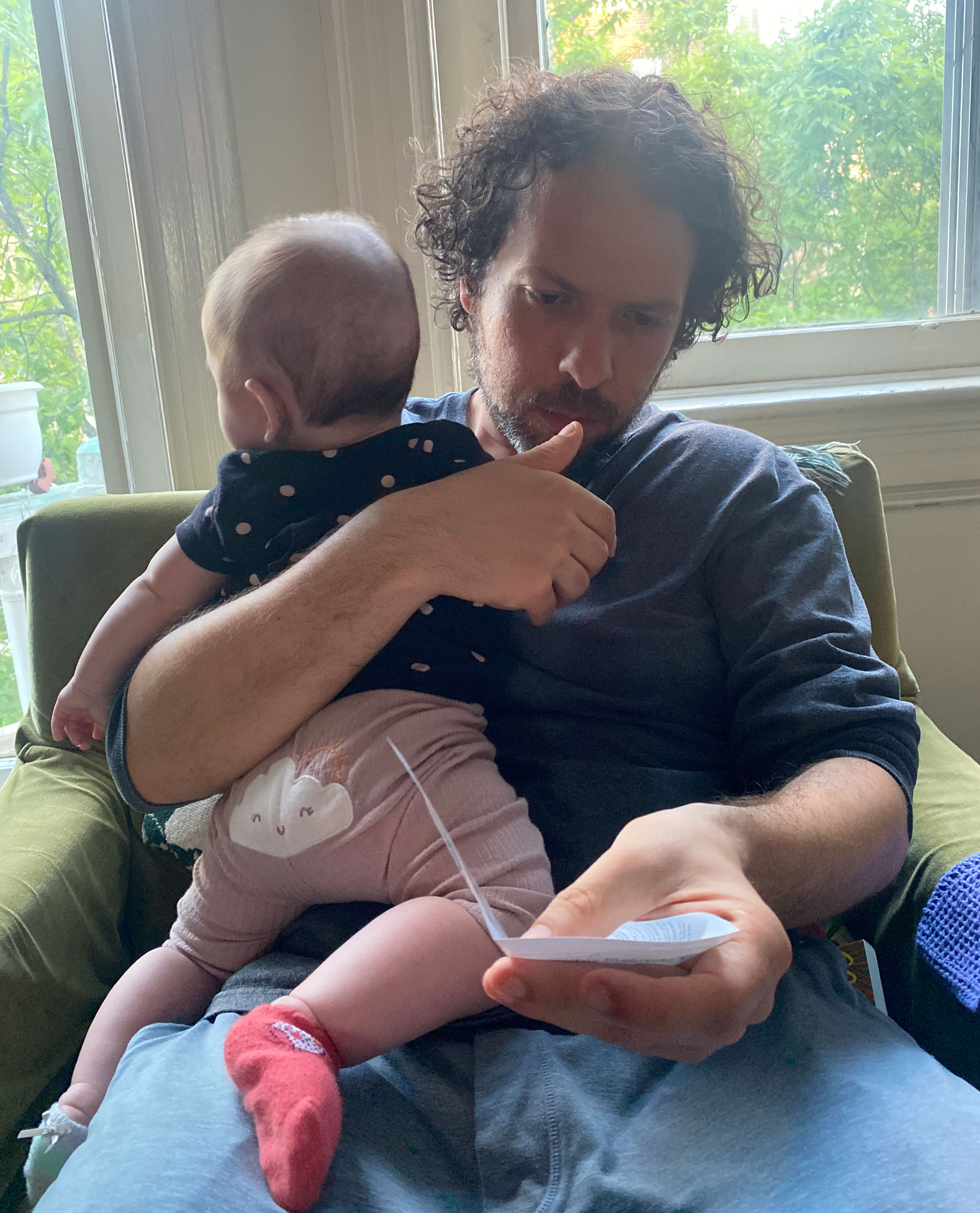 A photo of a father holding his infant daughter while reading an instruction manual in his other hand.