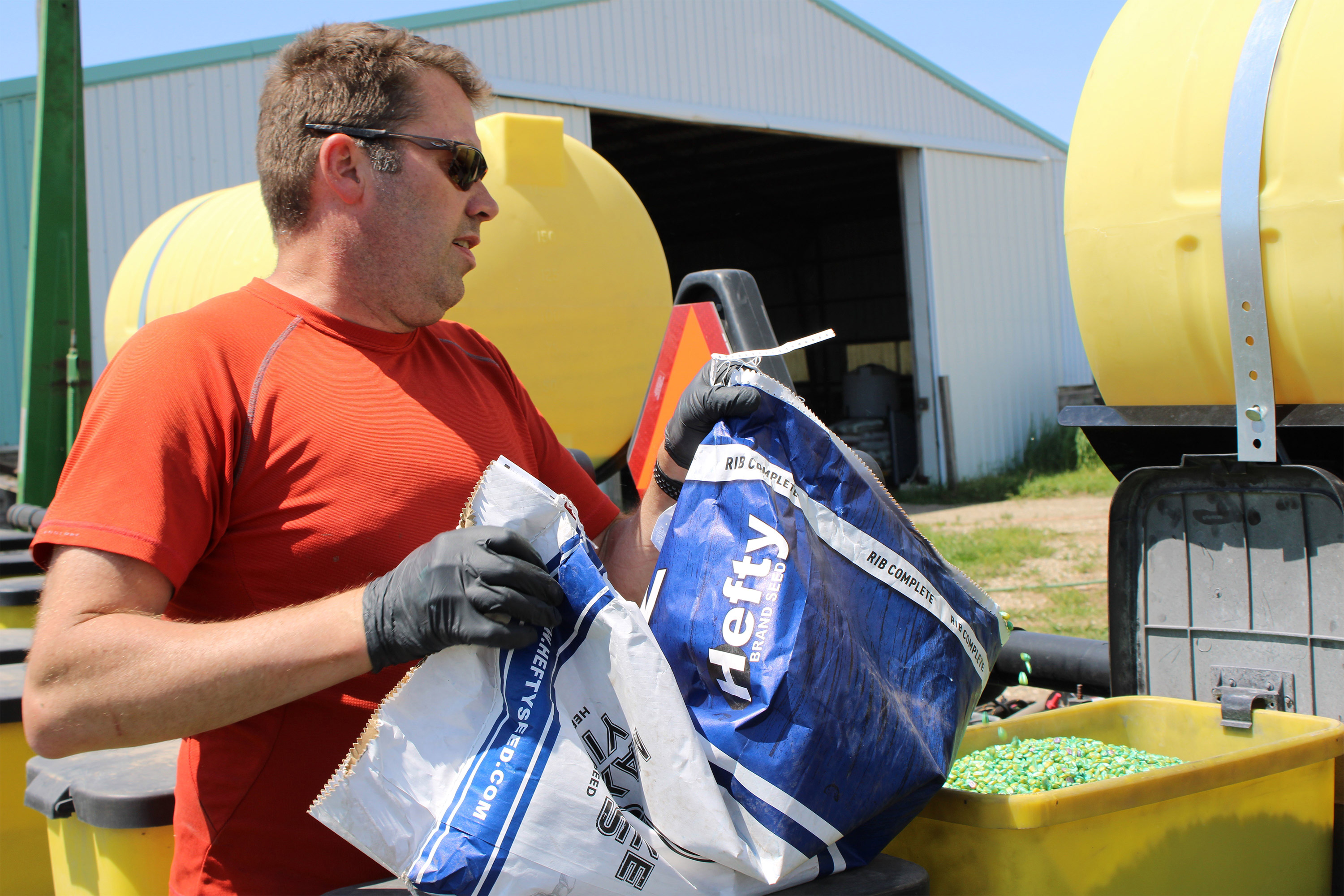 A photo of a farmer placing a seeds into a planter from a large bag.