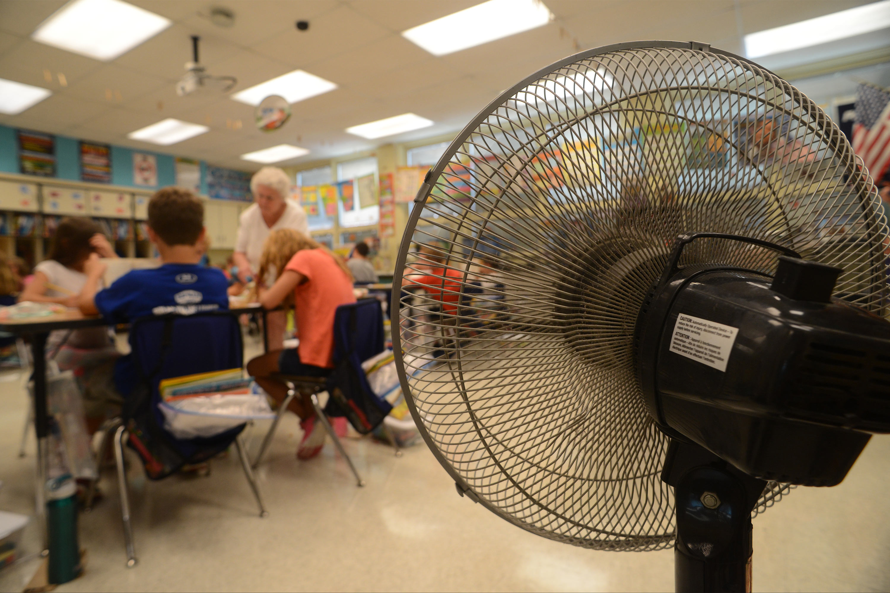 A photo of a fan setup in a classroom as a teacher helps students with their work.
