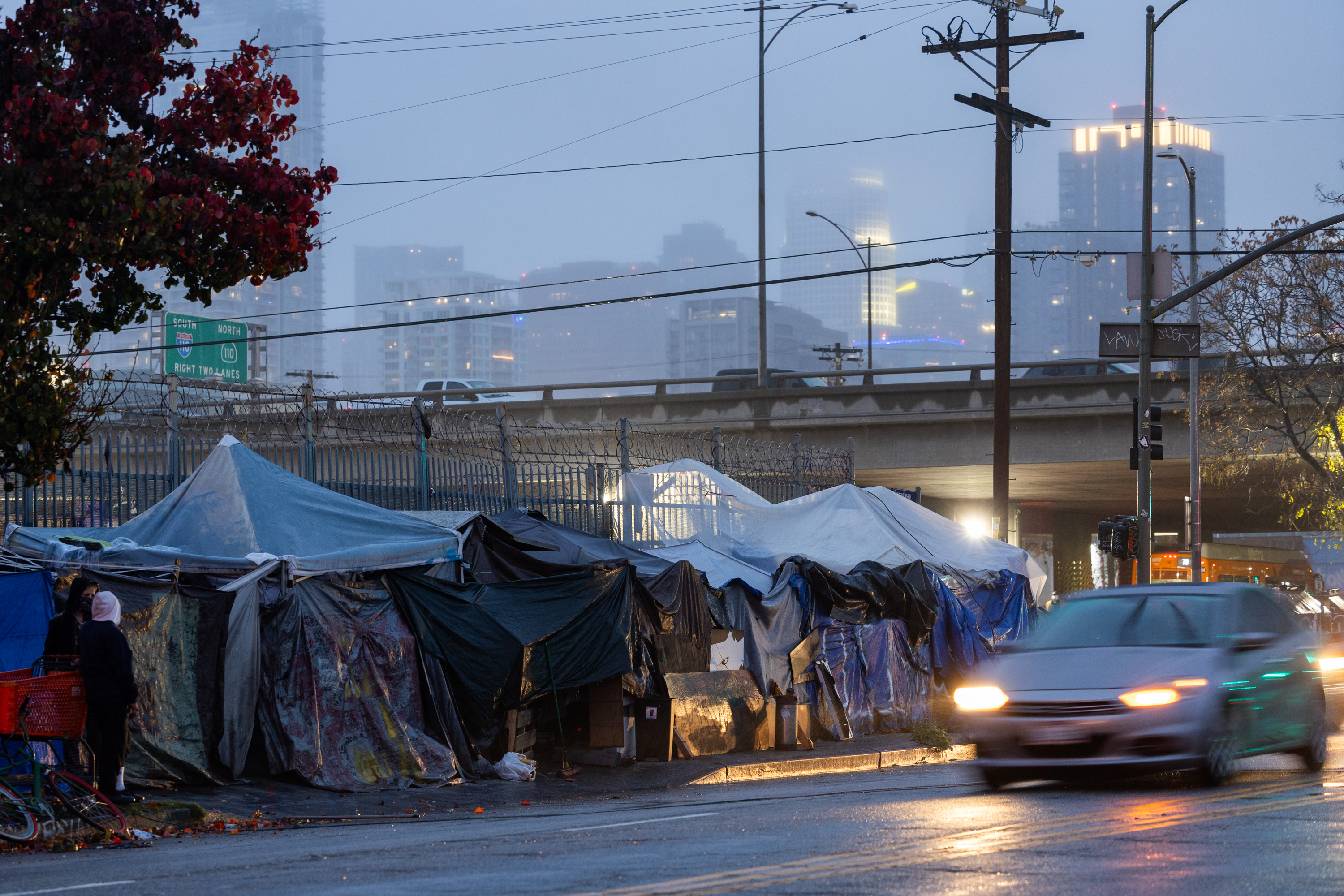 A photo of tents on the sidewalk next to a road with a car driving by.