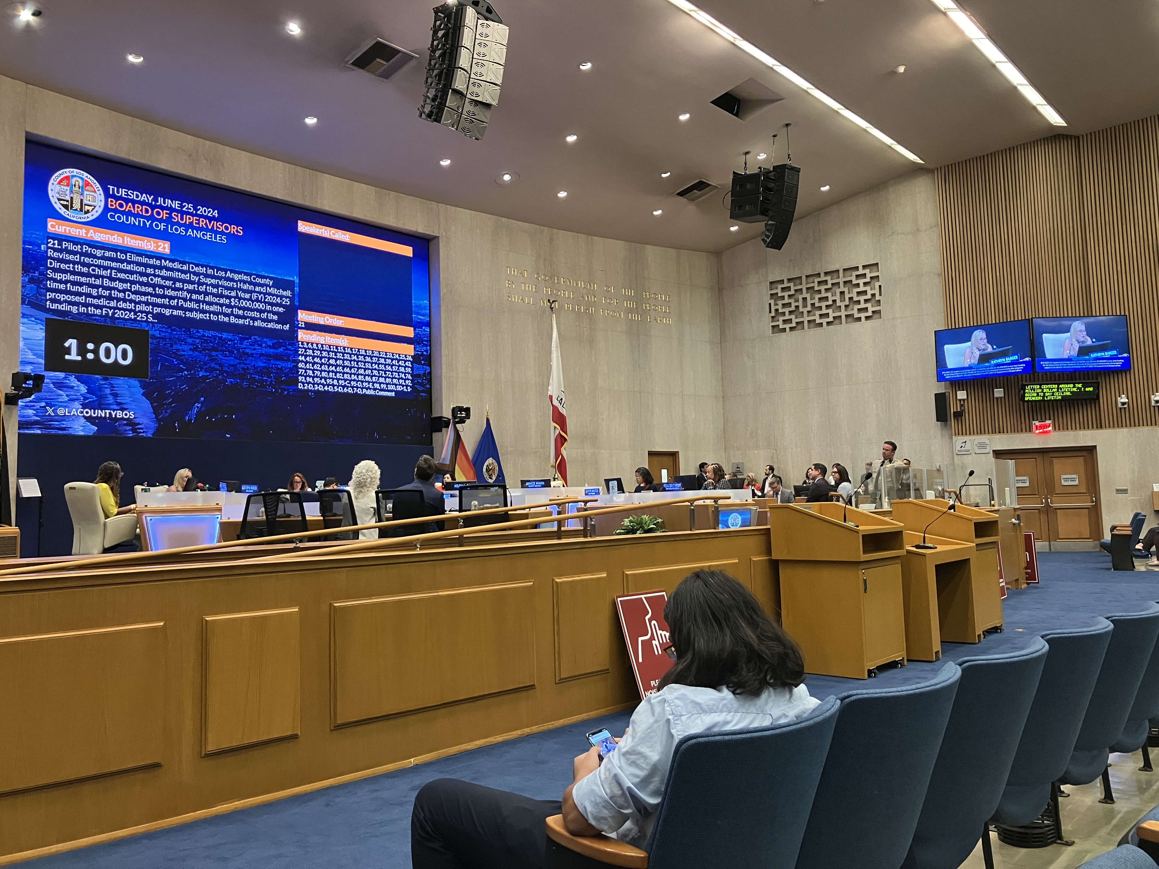 A court room with a large projector screen at the front. There are rows of blue chairs facing the screen.