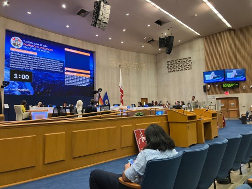 A court room with a large projector screen at the front. There are rows of blue chairs facing the screen.