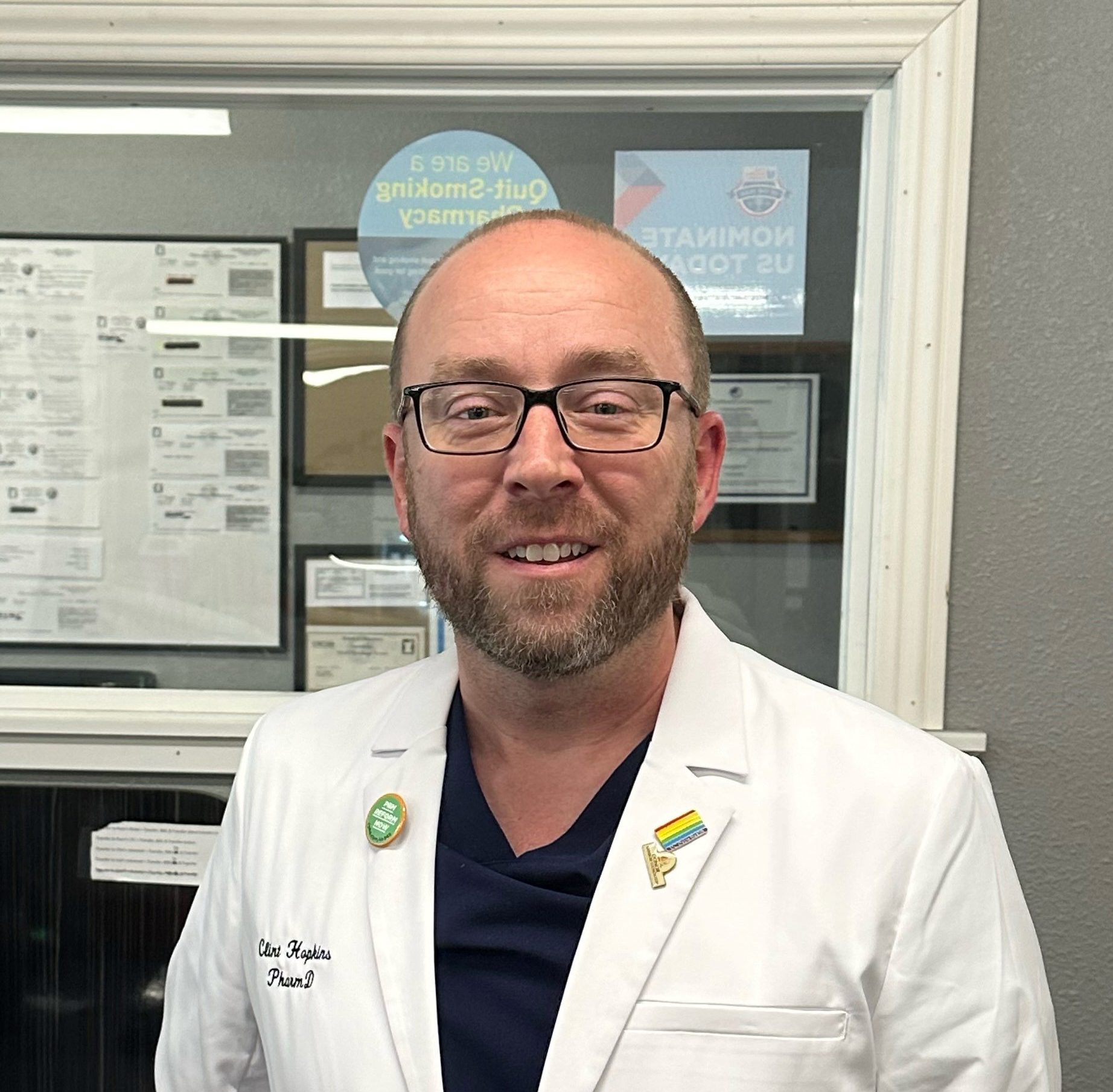 A photo of a man in a white pharmacist's coat smiling for a photo.