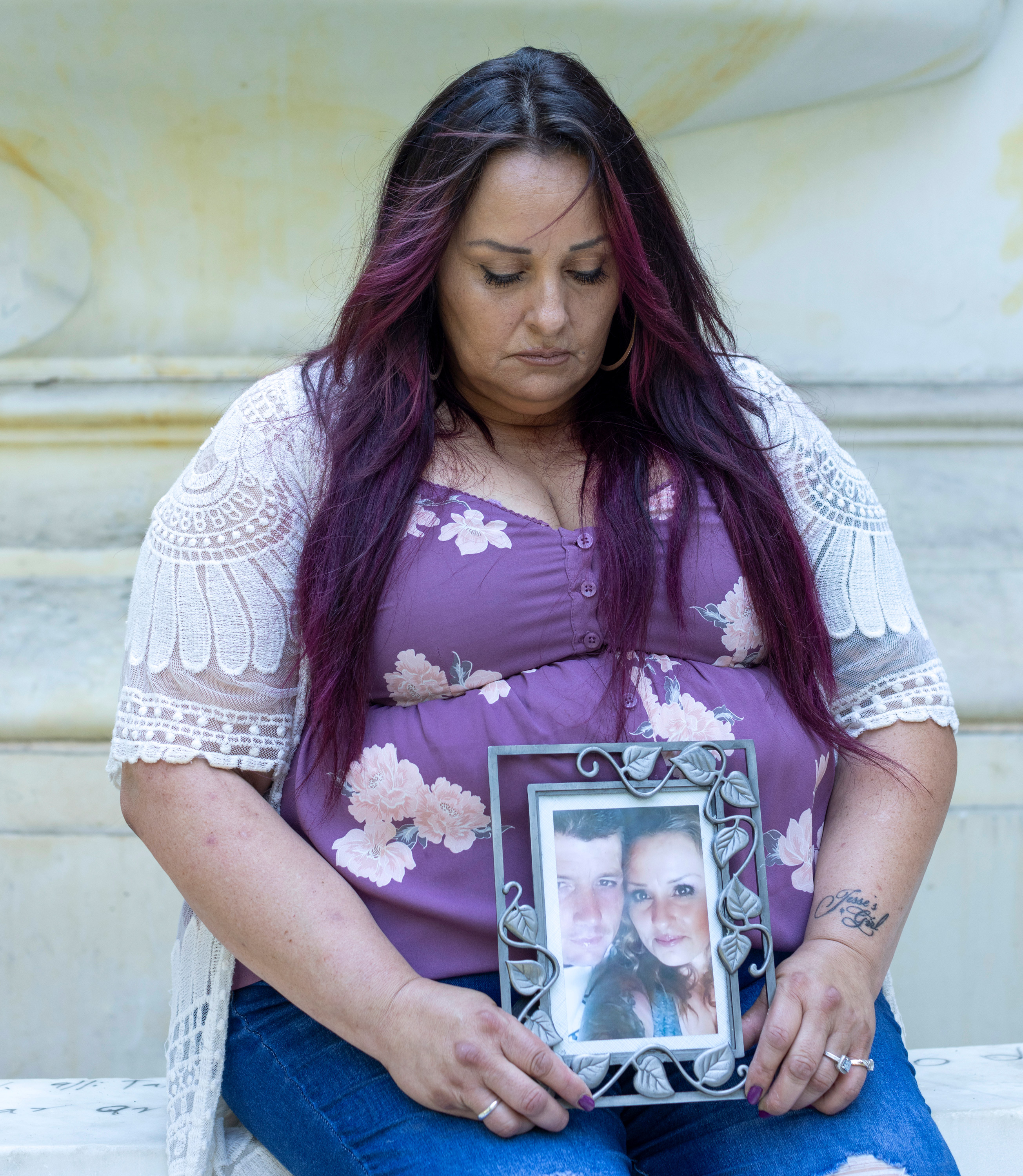 A portrait of Sonja Verdugo seated, looking down at a framed picture of herself with her deceased husband.