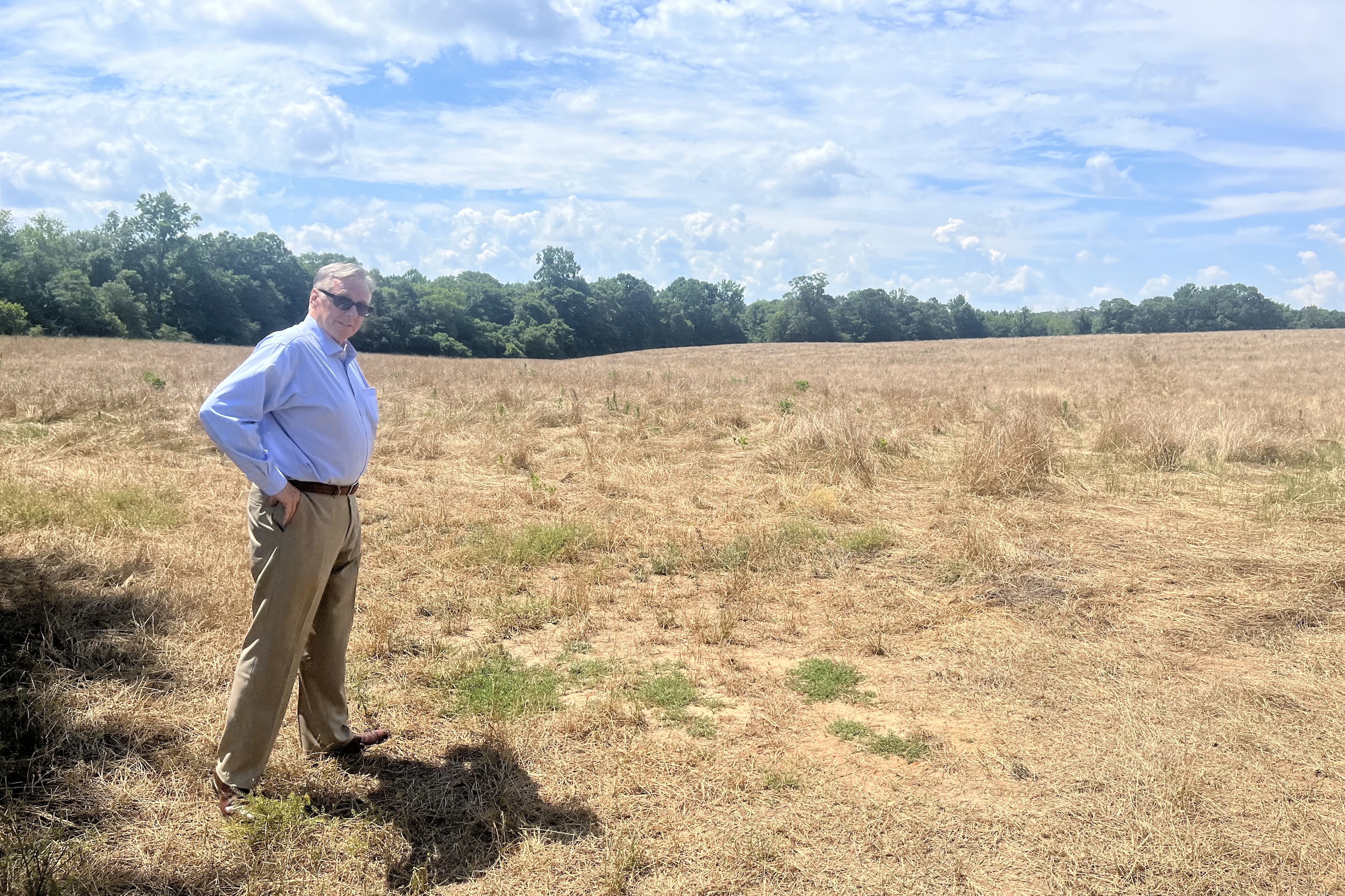 A man in a shirt and slacks stands in an empty field
