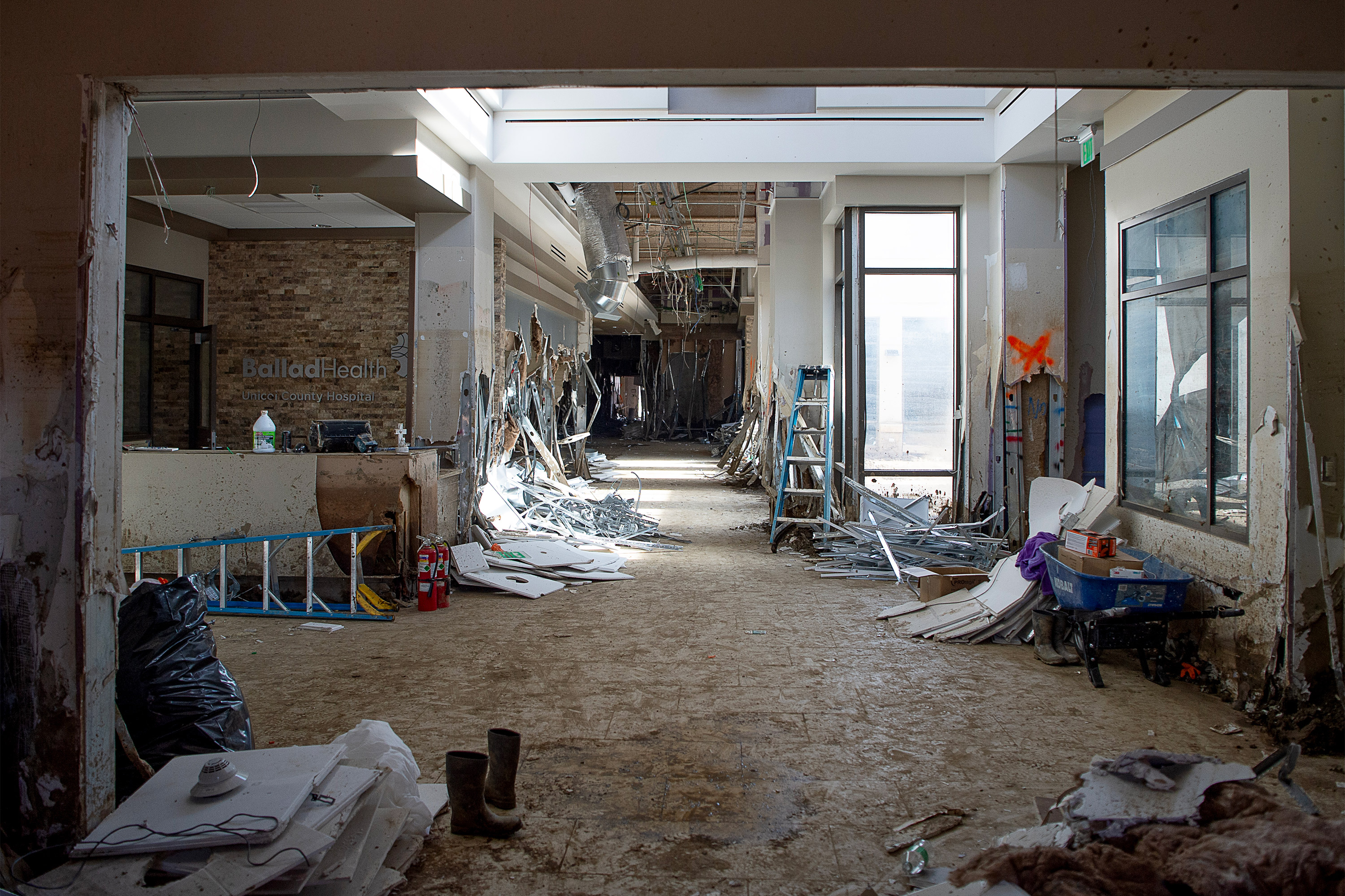 A photo of a hospital's front lobby in ruins. Paint is peeling off of the walls. Lights are dangling from the ceiling. 