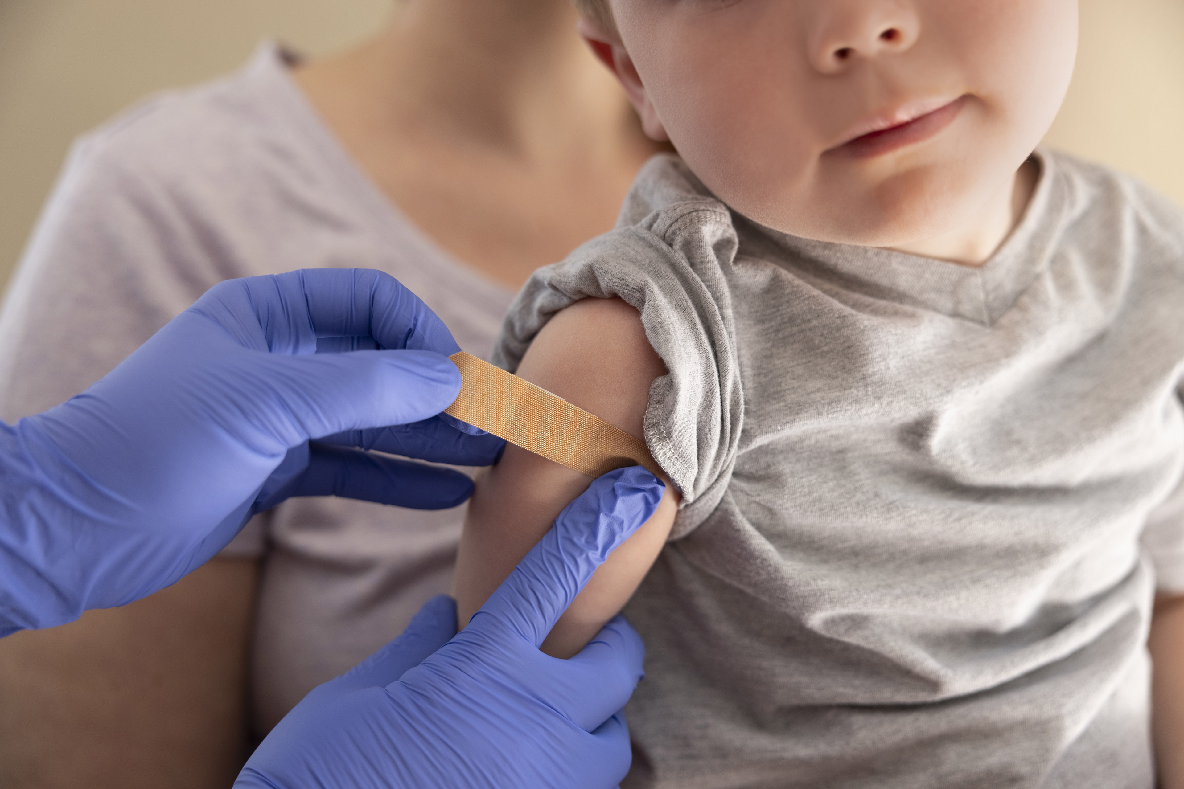 A close up photo of an unidentifiable toddler sitting in his mother's lap while a doctor puts a band-aid on his arm after receiving a vaccination.