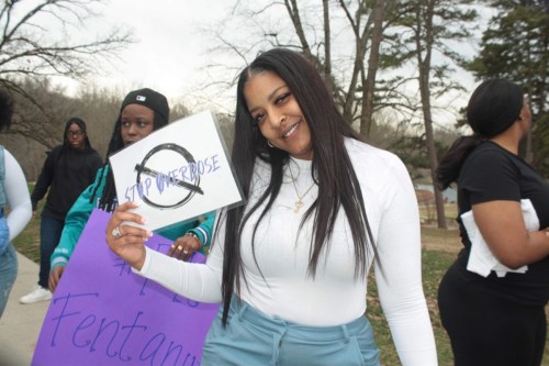 A photo of a Black woman posing for a photo while holding a sign that reads, "Stop overdose." Others hold signs behind her.