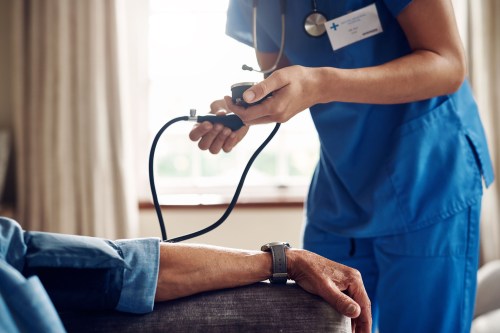 A photo of a senior man having his blood pressure checked during a visit with a health care professional at his home.