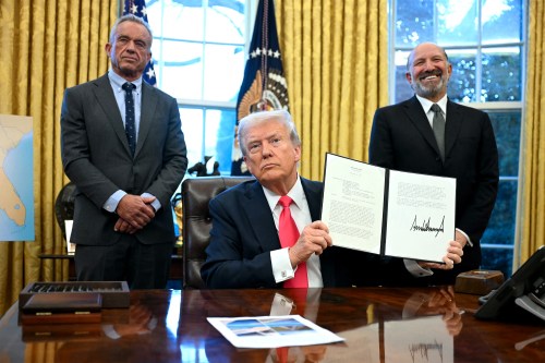 A photo of President Trump showing a signed executive order to photographers in the Oval Office of the White House. He is flanked by Robert F. Kennedy Jr. and Howard Lutnick.