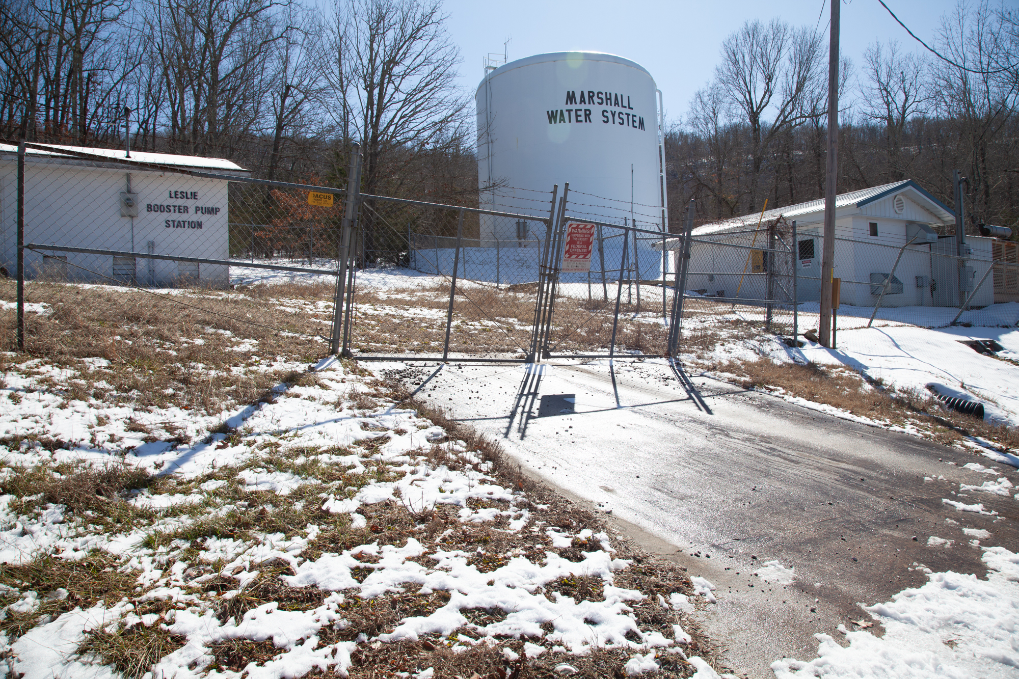 A photo of water tank labeled "Marshall Water System" seen behind a fence.