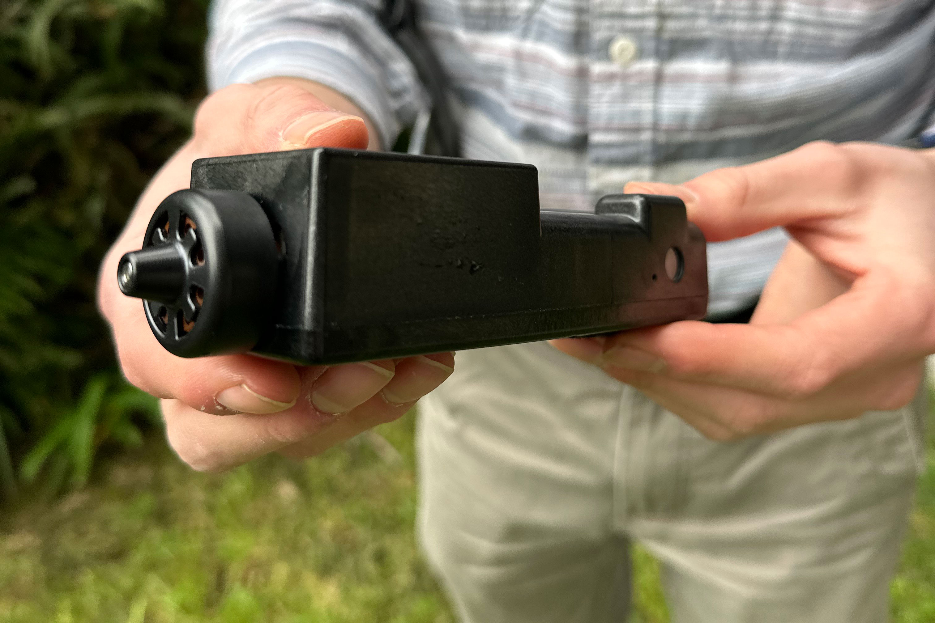 A close-up image of black device in the hands of a person standing outside.