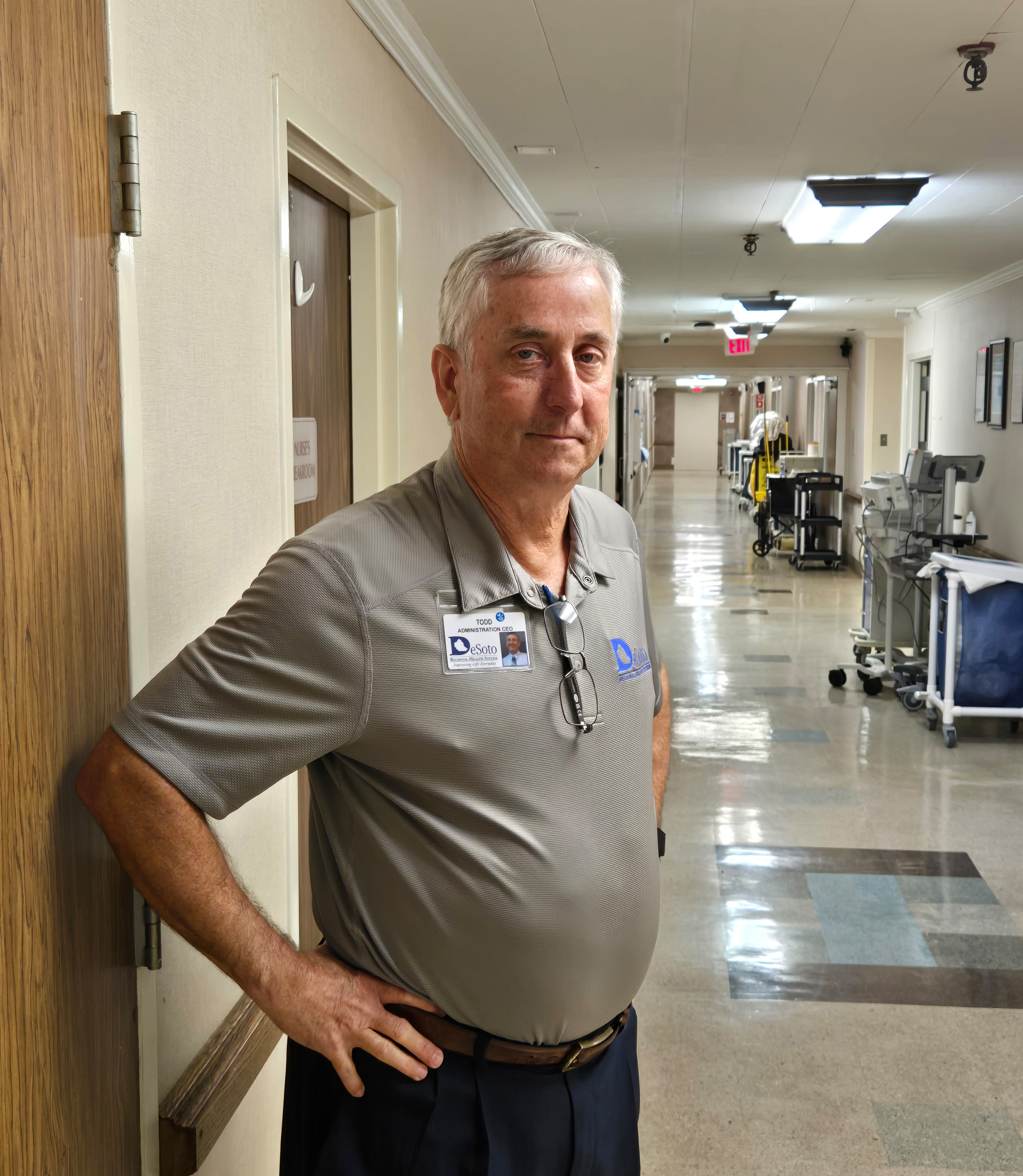 A photo of an older man standing for a portrait in a hospital corridor.