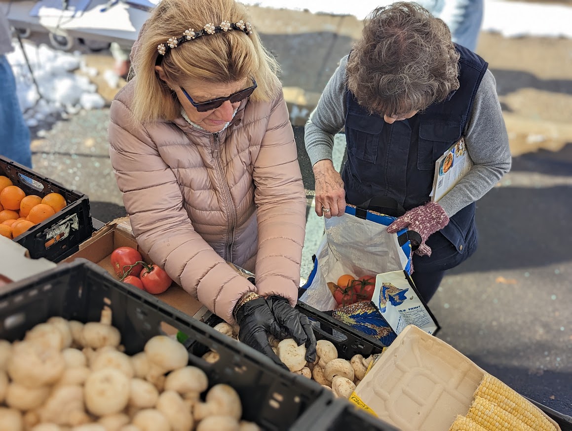 A photo of two women filling up bags of tomatoes and mushrooms.