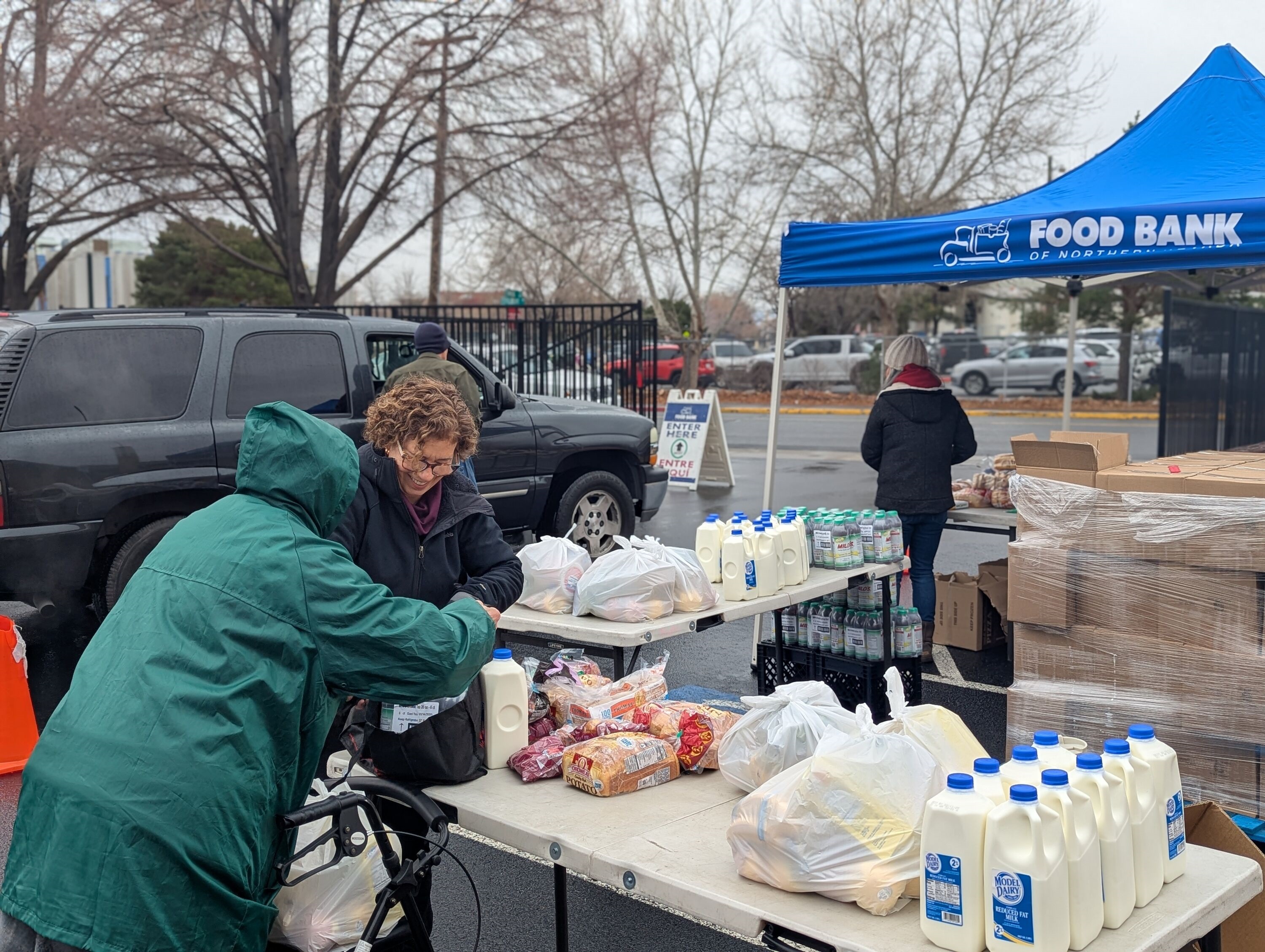 A photo of food bank attendees picking up loaves of bread, half-gallons of milk, and bags of produce.