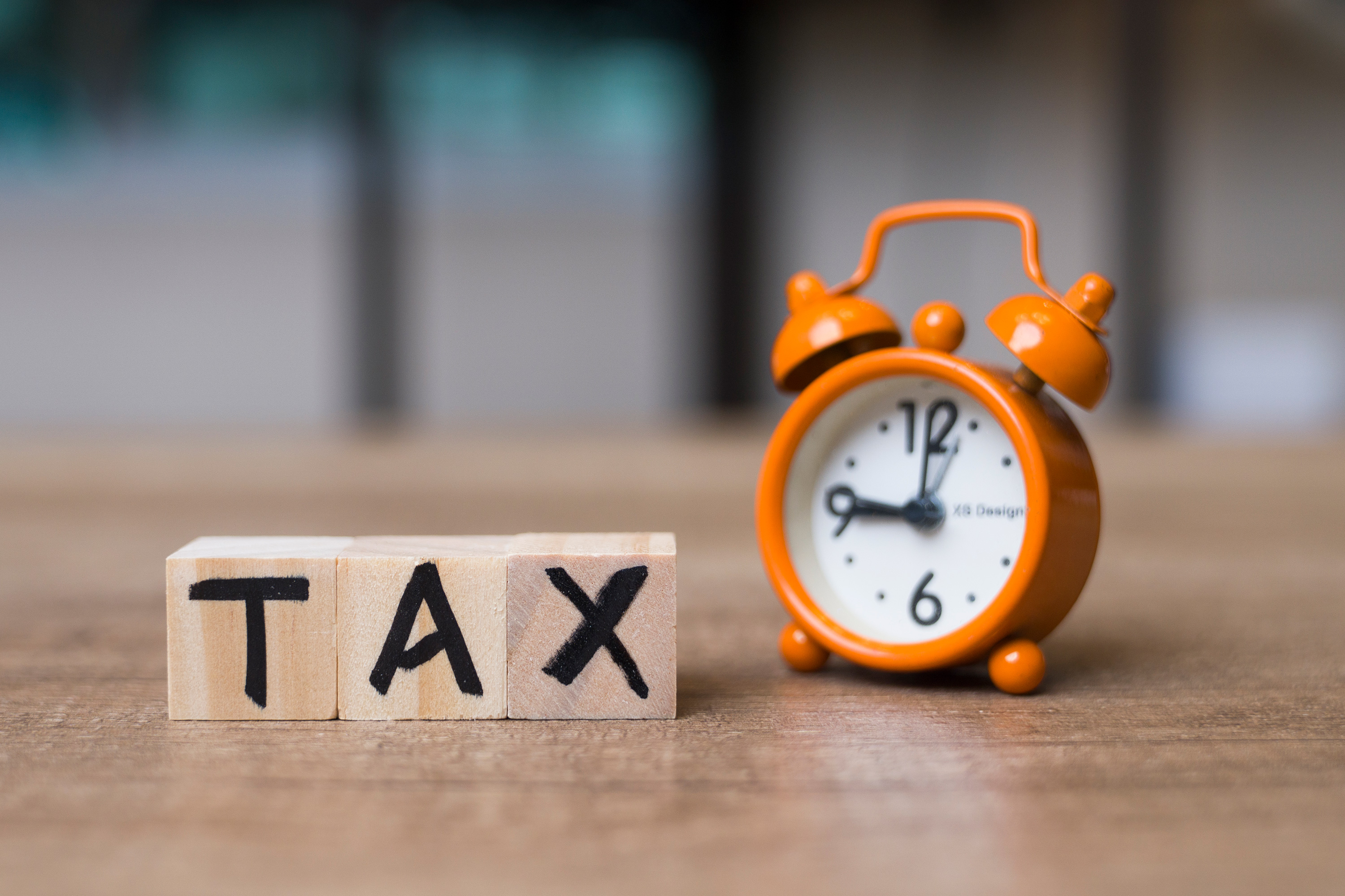 A photo of an alarm clock on a desk next to blocks with the letters "T-A-X" written on them.