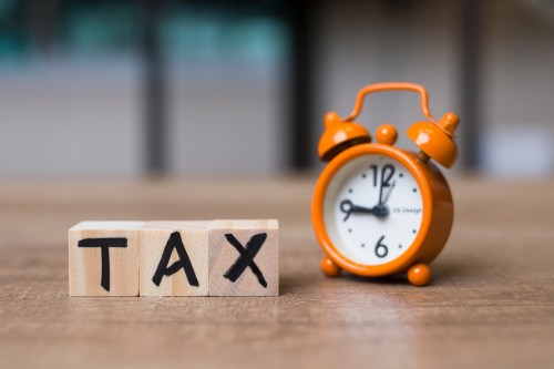 A photo of an alarm clock on a desk next to blocks with the letters "T-A-X" written on them.