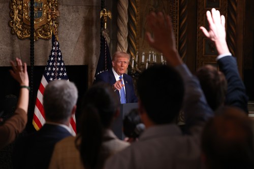 Donald Trump is pictured from afar. The raised hands of reporters are seen in the foreground.