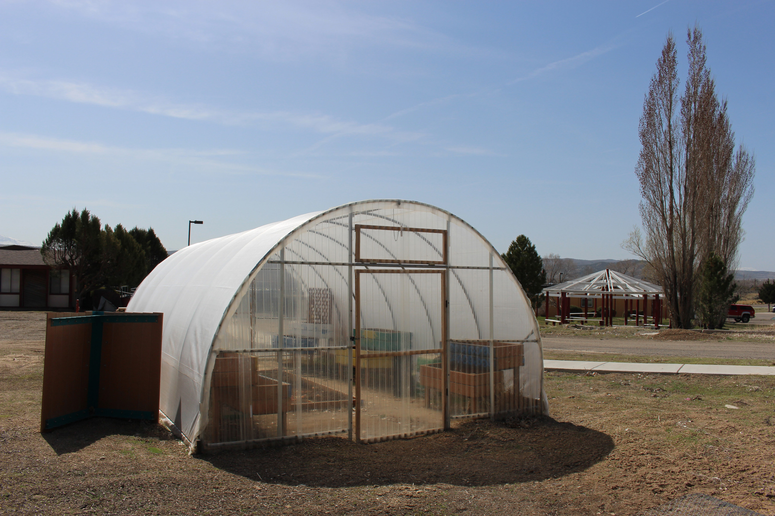 A photo of a hoop house, a structure similar to a greenhouse, with rounded hoops supporting the structure and clear tarps trapping heat inside of it for growing plants.