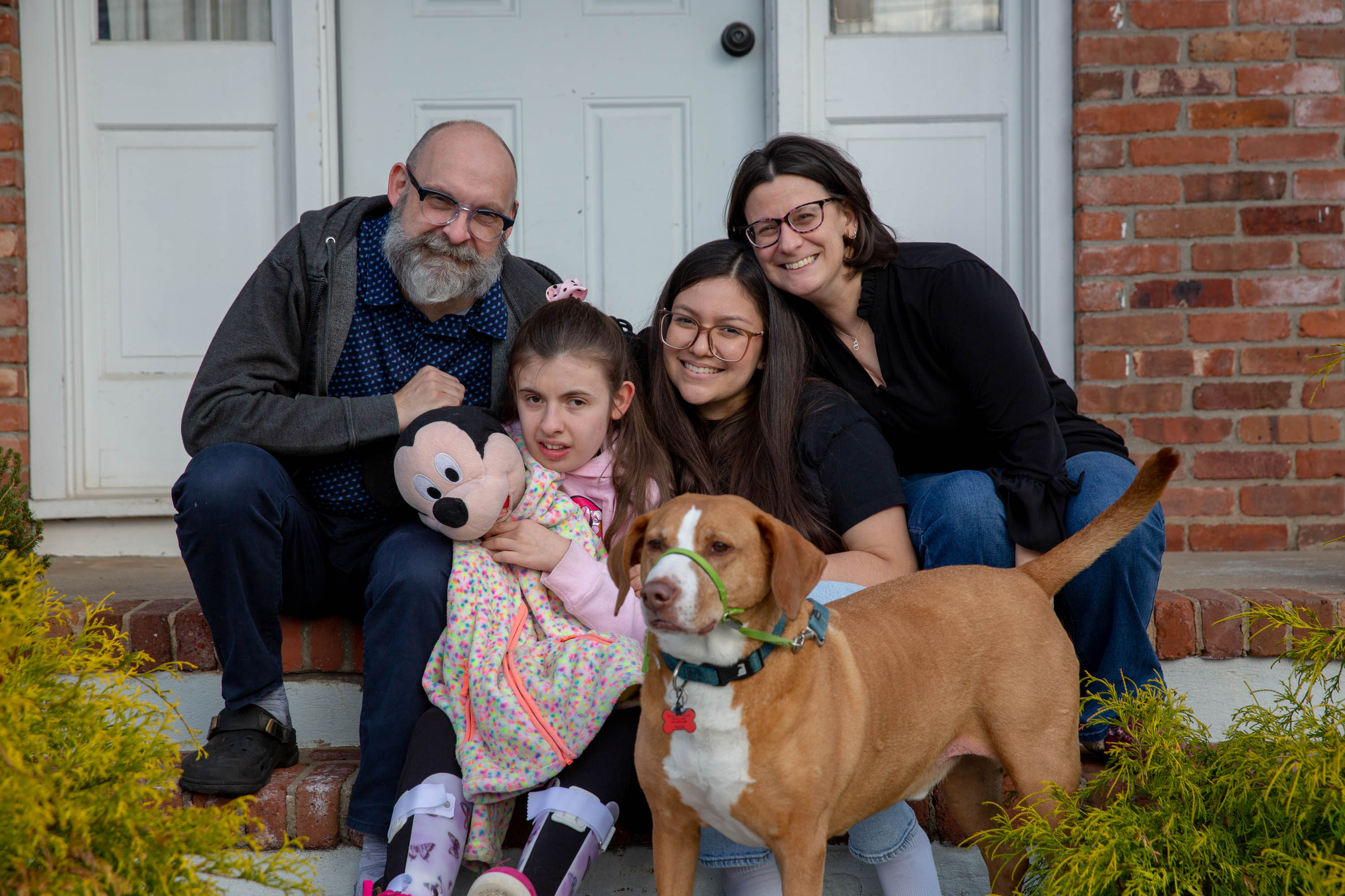 A group of people sits on the front step of a home, posing for a portrait, with a dog