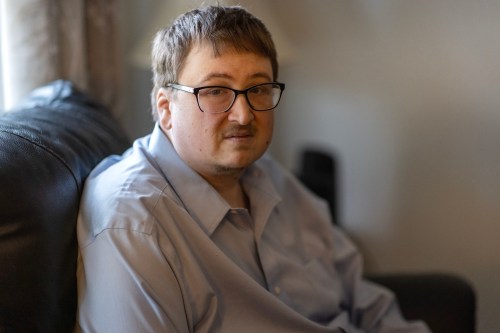 A man wearing glasses sits on a couch facing the camera.