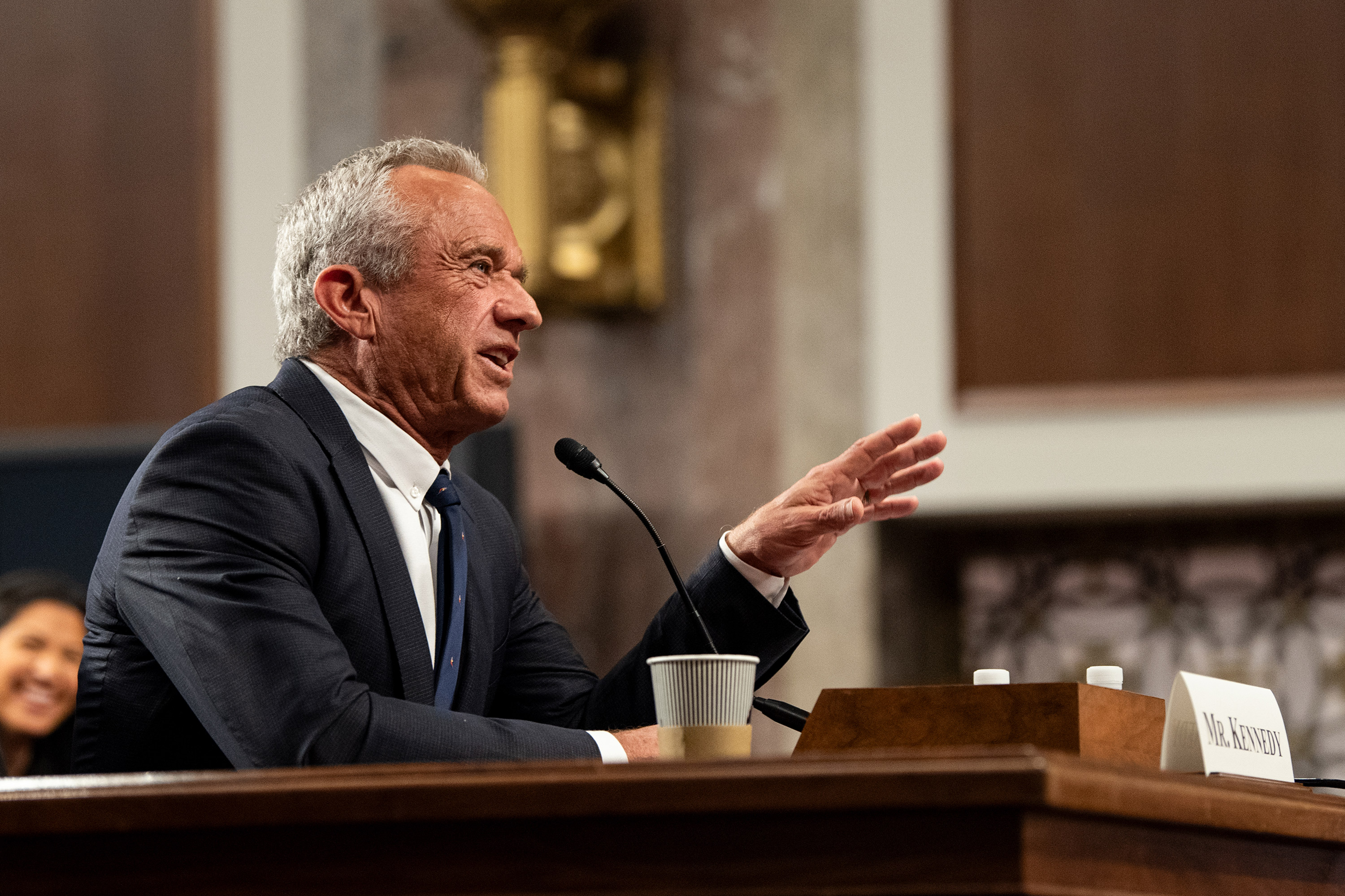 A photo of Robert F. Kennedy Jr. speaking into a microphone in a Senate hearing room.