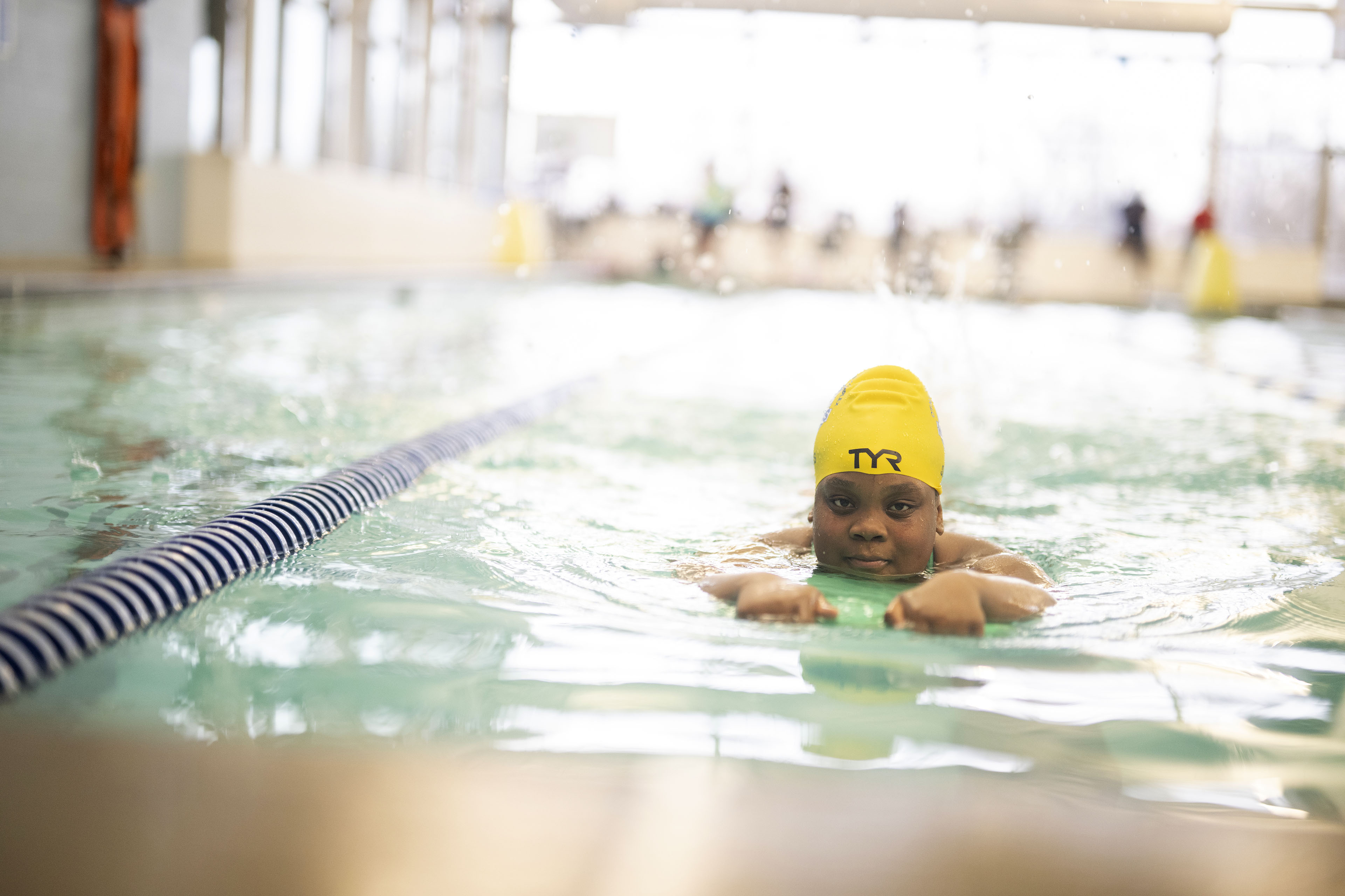 A girl wearing a yellow swim cap swims laps in a pool lane