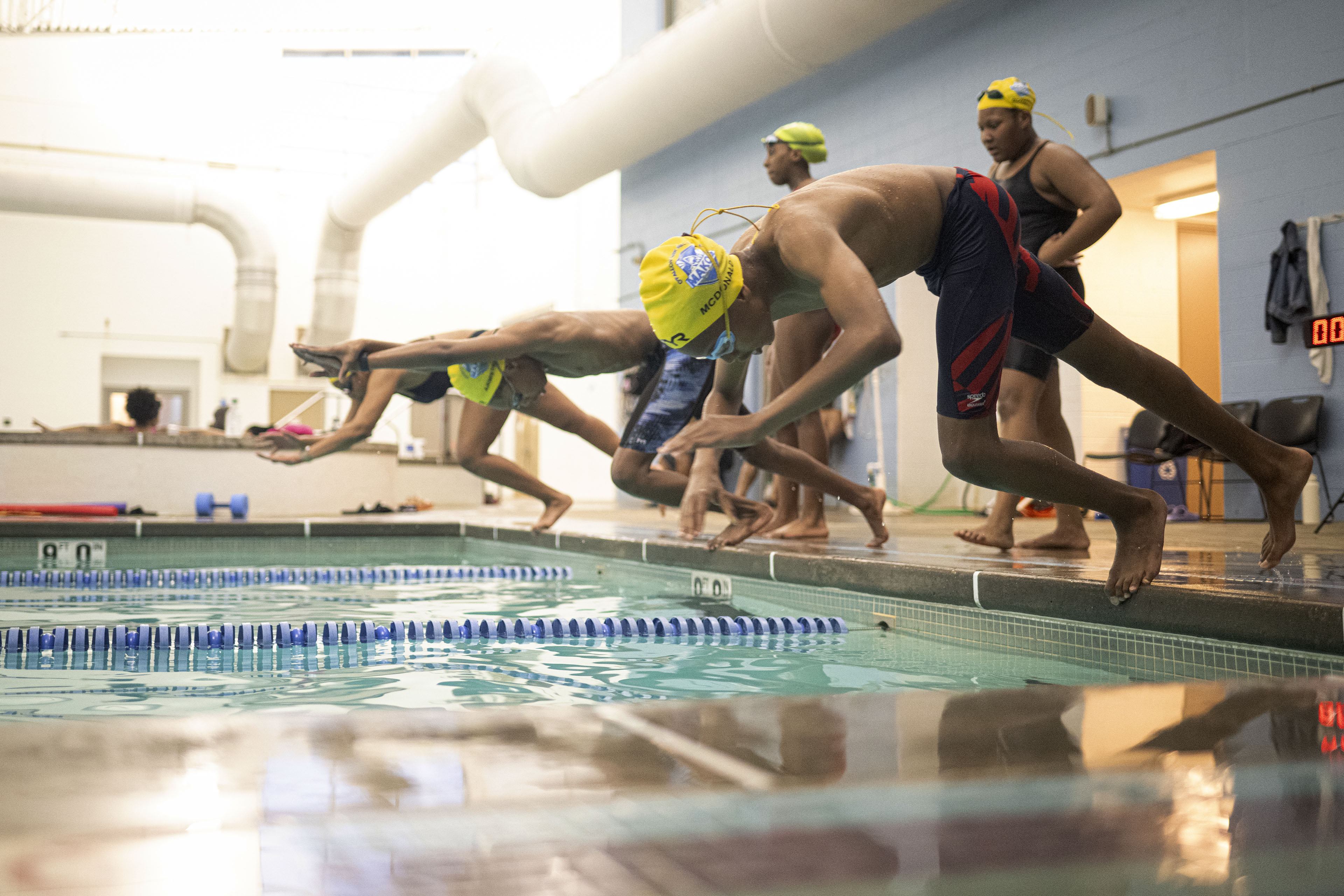 Three kids dive into a pool with lanes as two others watch