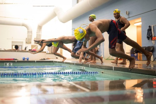Three kids dive into a pool with lanes as two others watch