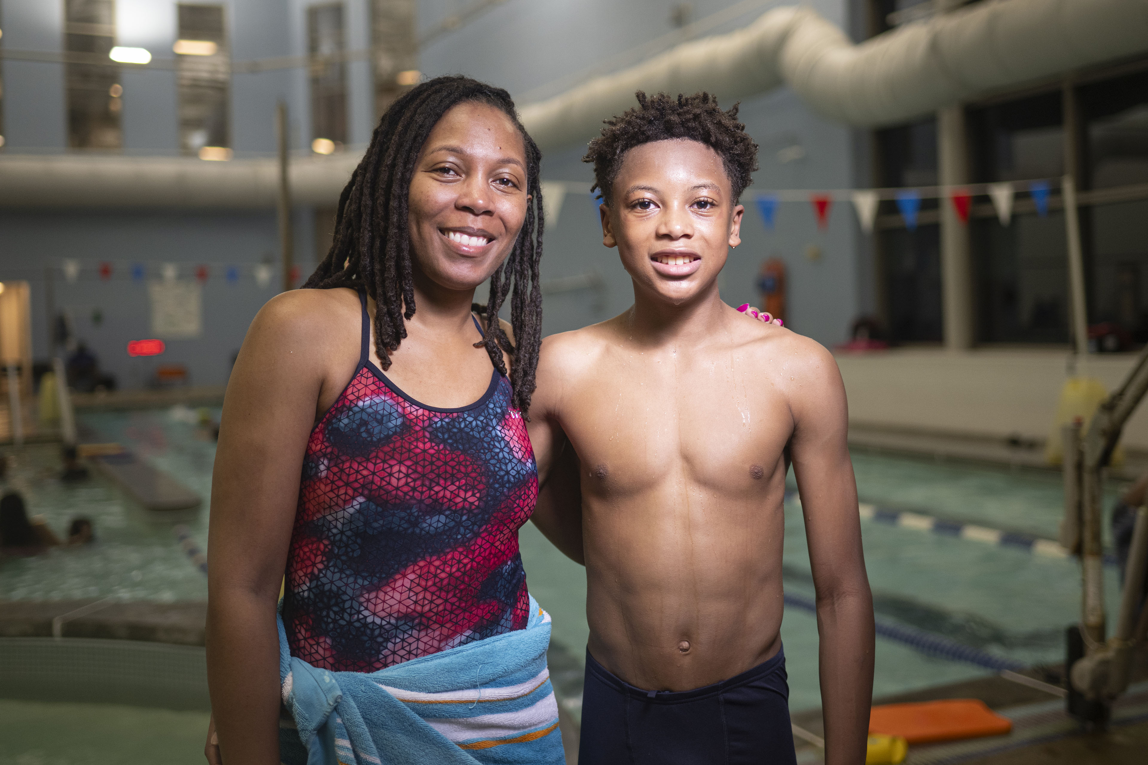 A woman wearing a blue and pink bathing suit poses for a portrait with a boy in front of a pool