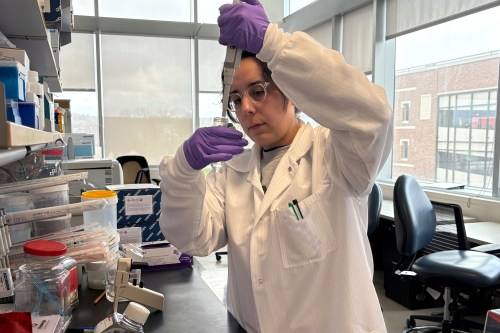A photo of a woman in a lab coat using a pipette and flask.