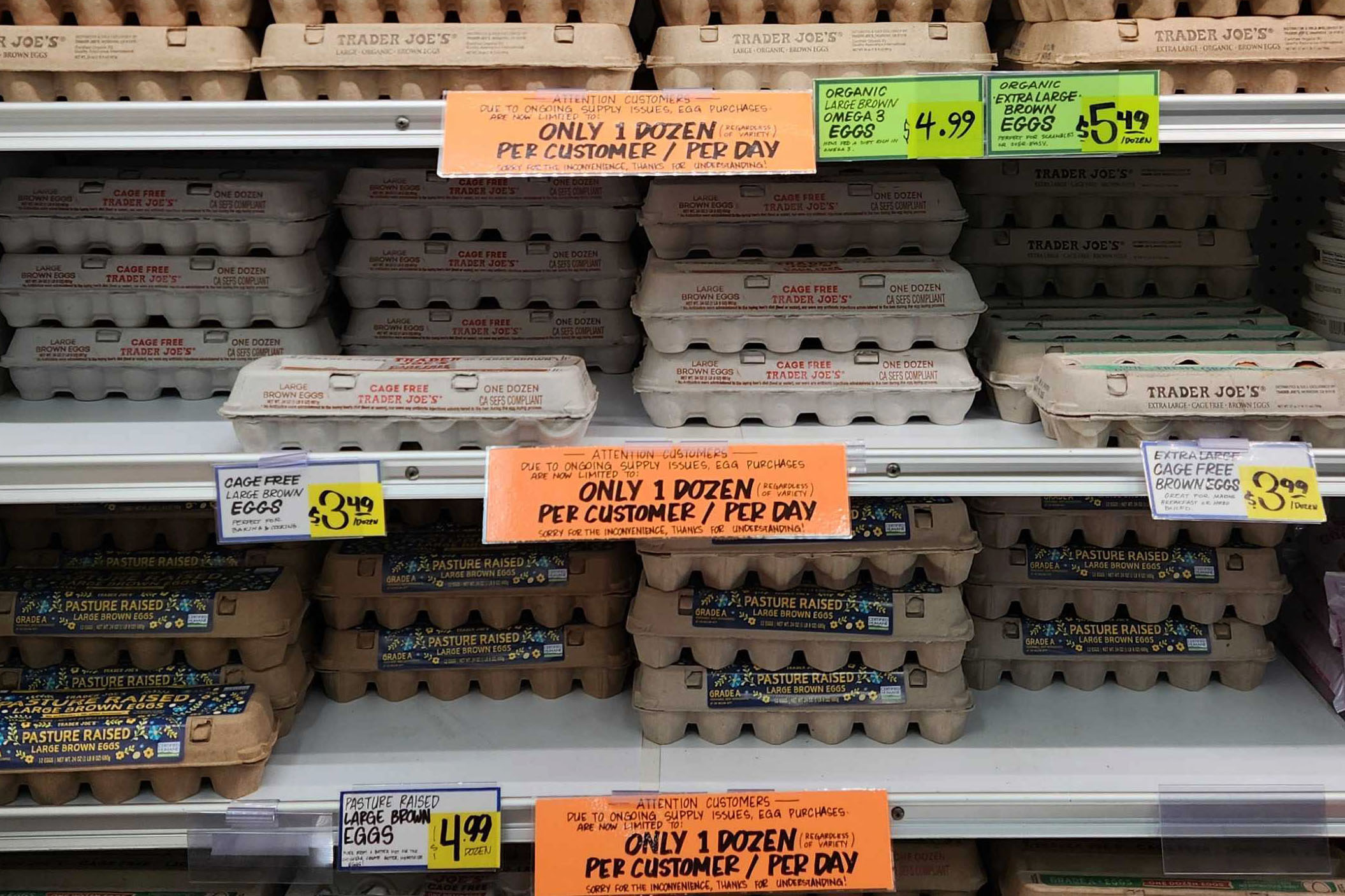 A photo of eggs on shelves at a Trader Joe's. There are orange signs on each shelf that say, "Only 1 dozen per customer / per day."