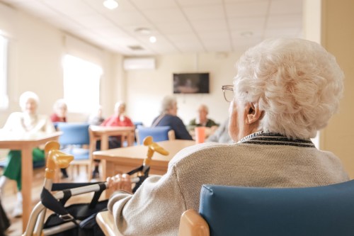 A photo of an elderly woman sitting with her walker in the common area of a nursing home.
