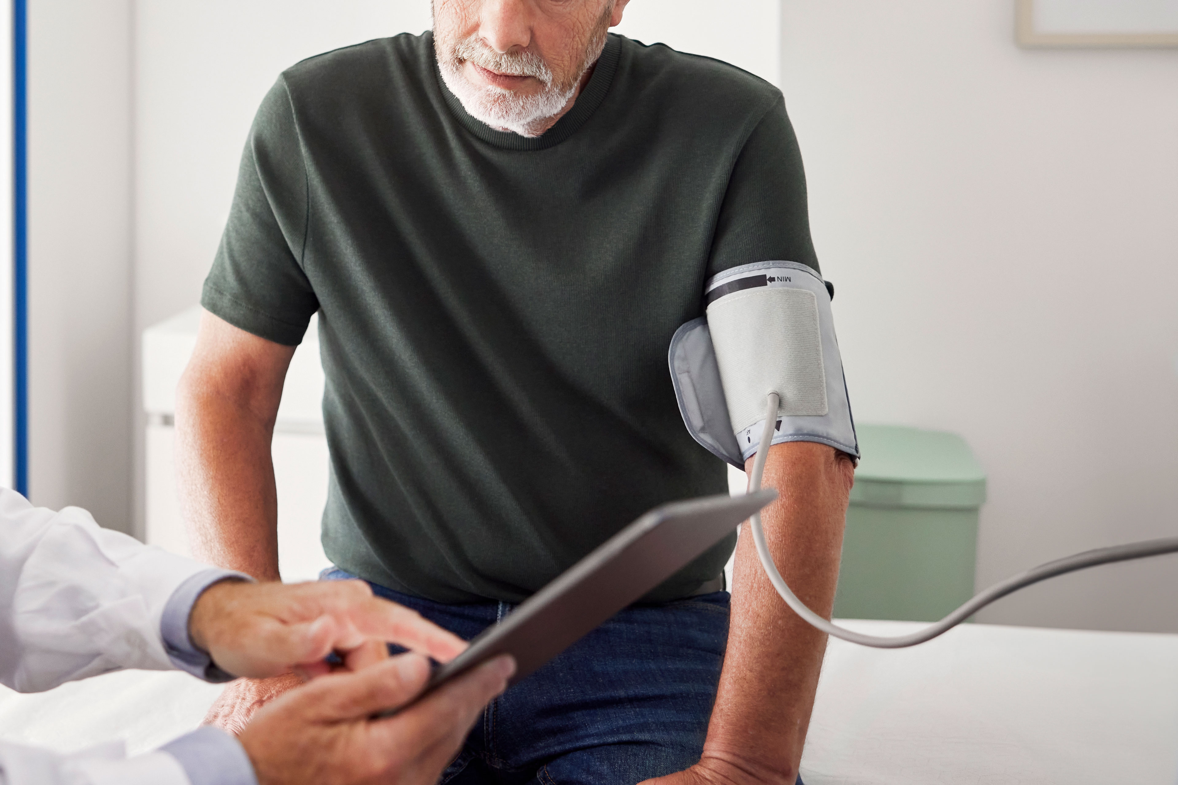 A photo of an older man having his blood pressure checked by a doctor in an exam room.
