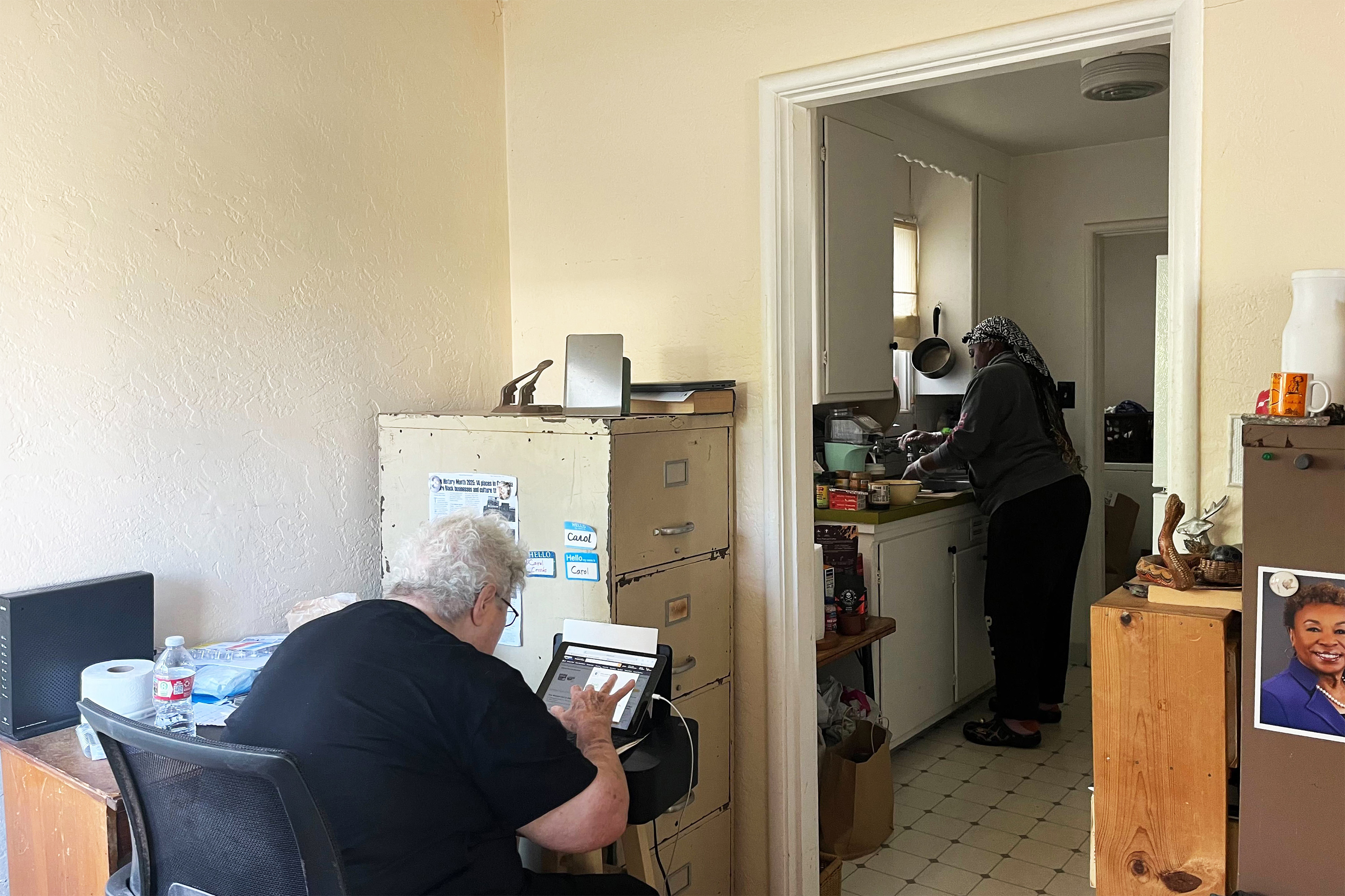 A photo of Florence Owens at the kitchen sink while Carol Crooks works at a computer.