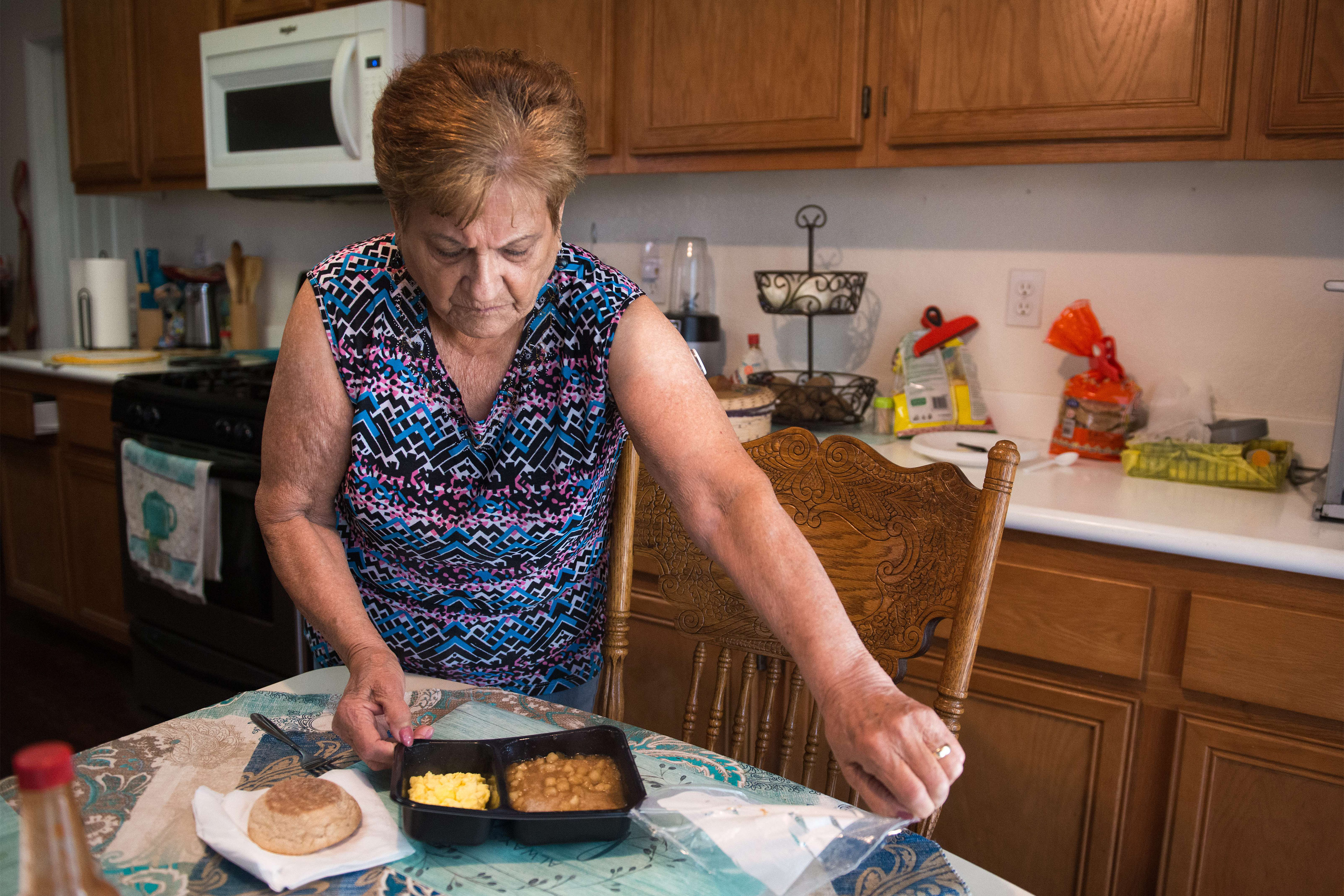 A photo of a woman peeling plastic off of a frozen meal.