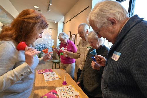 A photo of a woman leading a group of older adults in a game with hand bells.