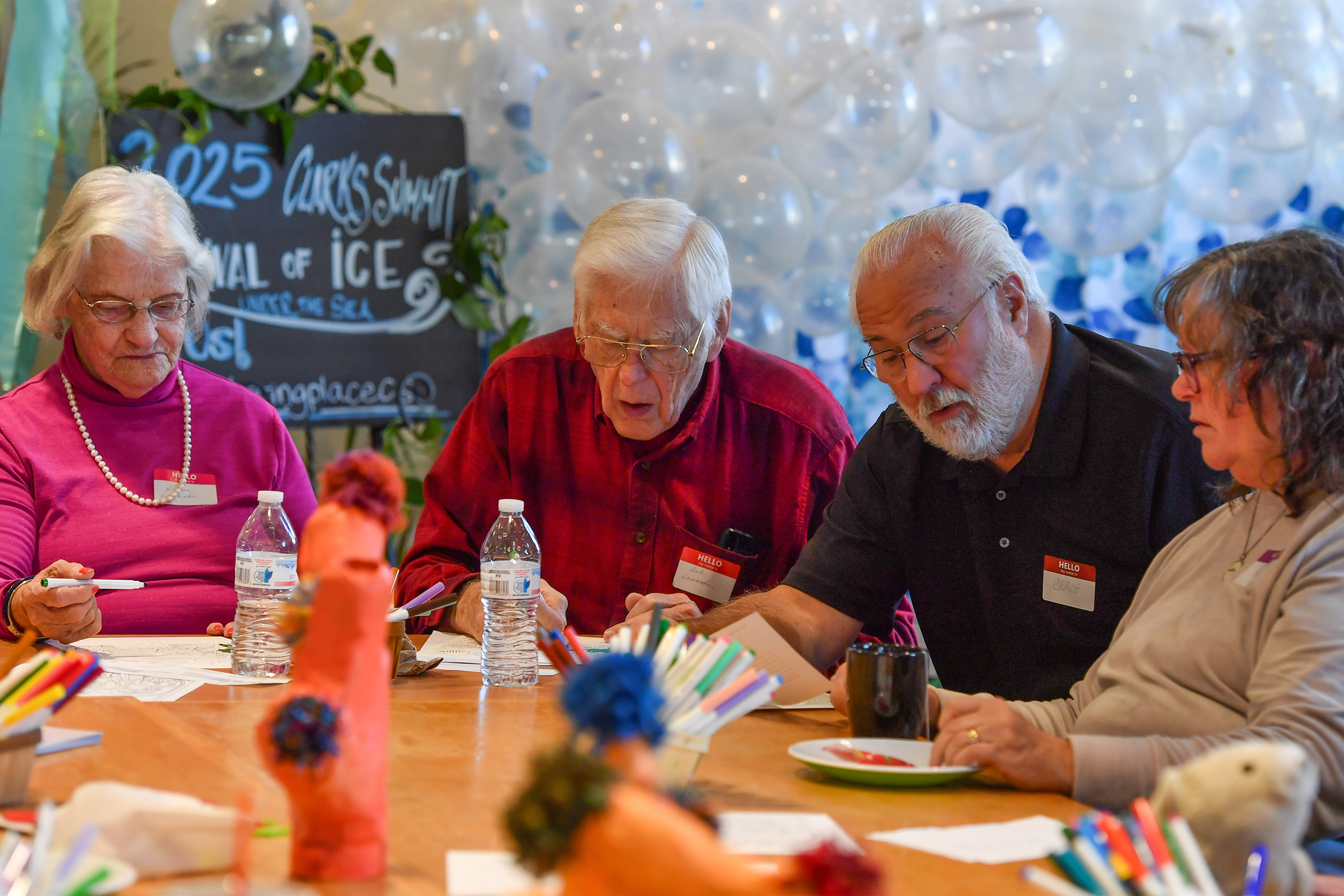 A photo of a group of older adults seated at a table filling in coloring pages with markers.