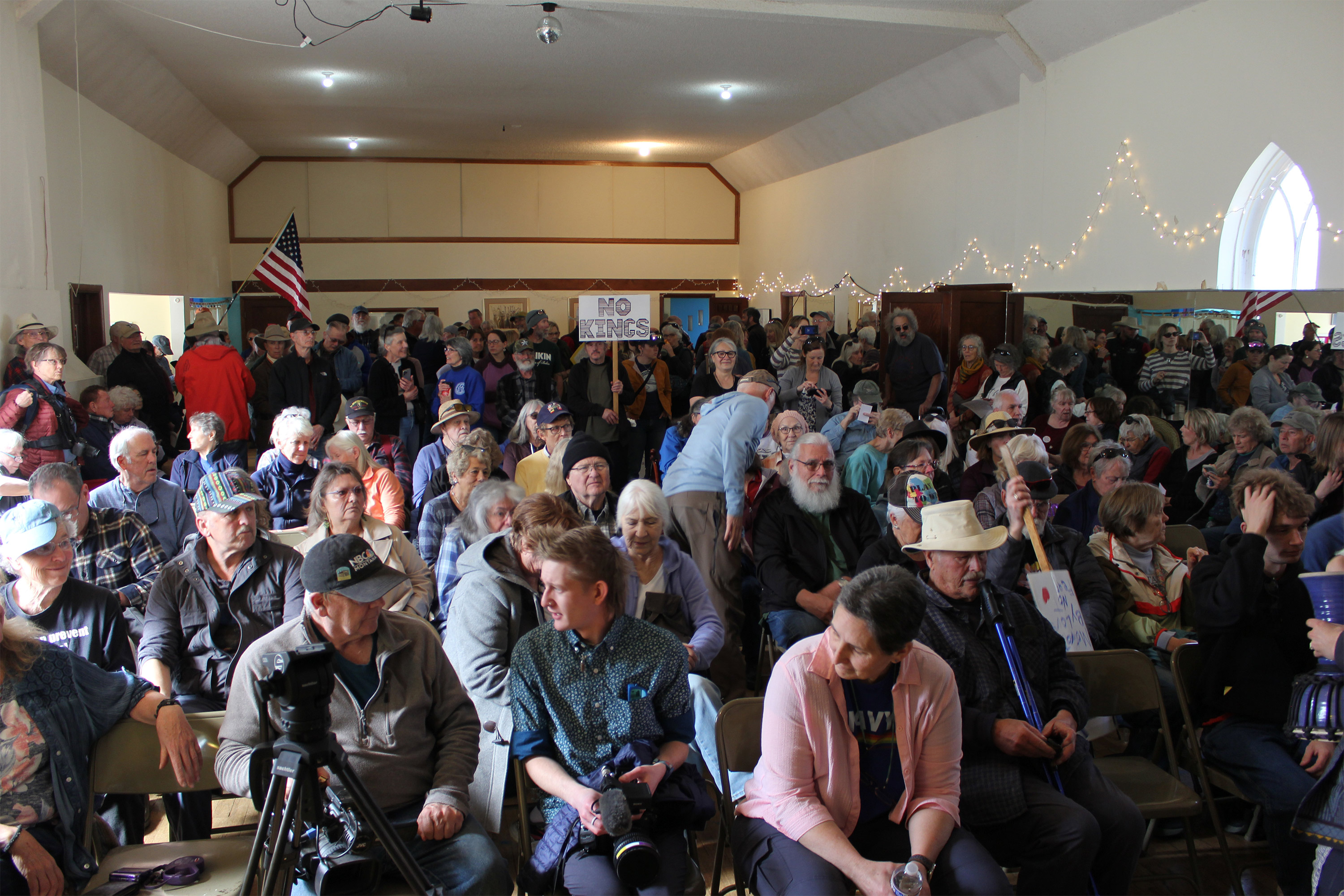 A photo of a crowded meeting room filled with protesters sitting in chairs.