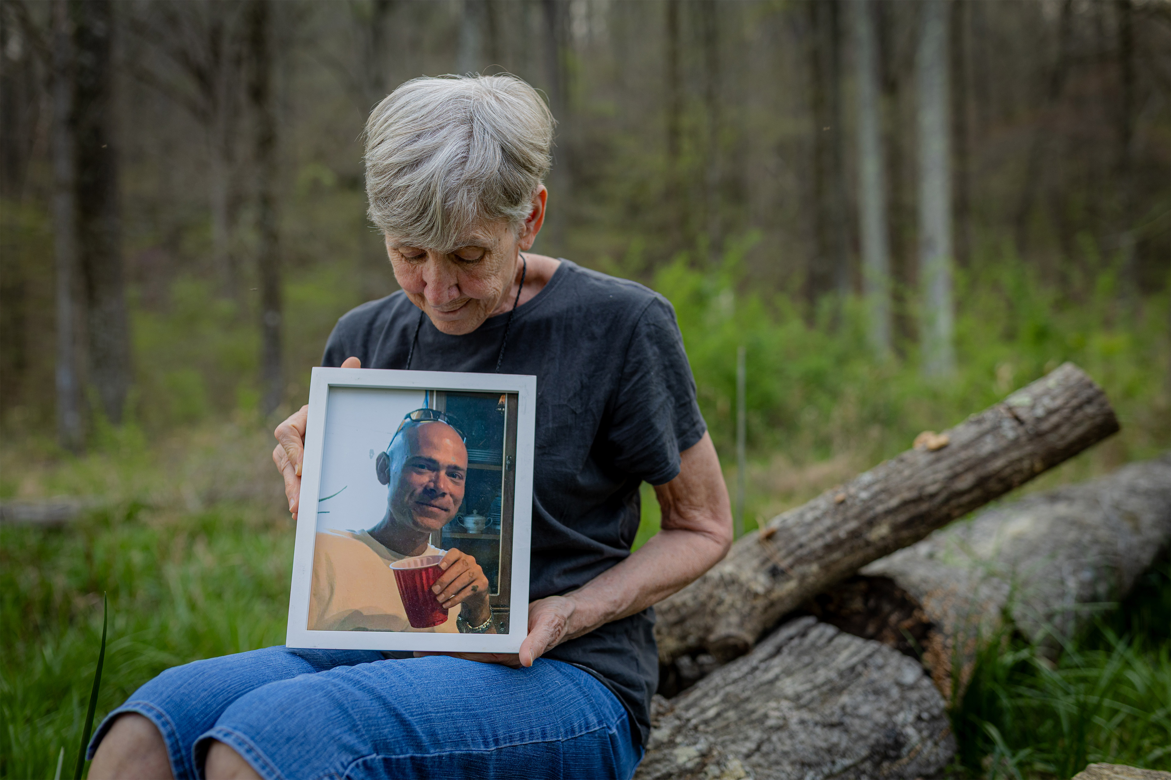 A photo of an older woman seated outside, holding and looking down at a picture of her adult son.
