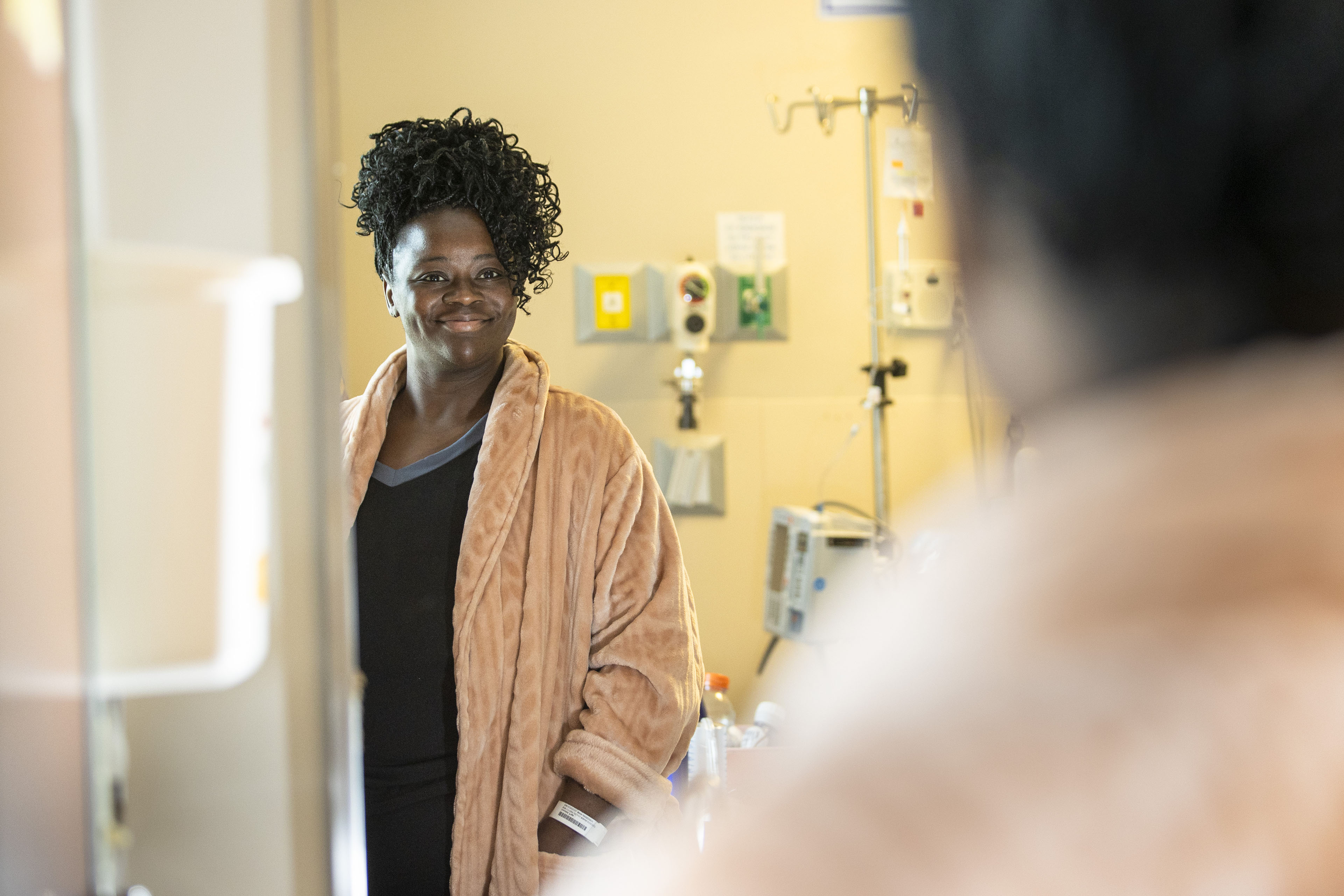 A photo of a woman in a hospital room facing a mirror and smiling at her reflection.