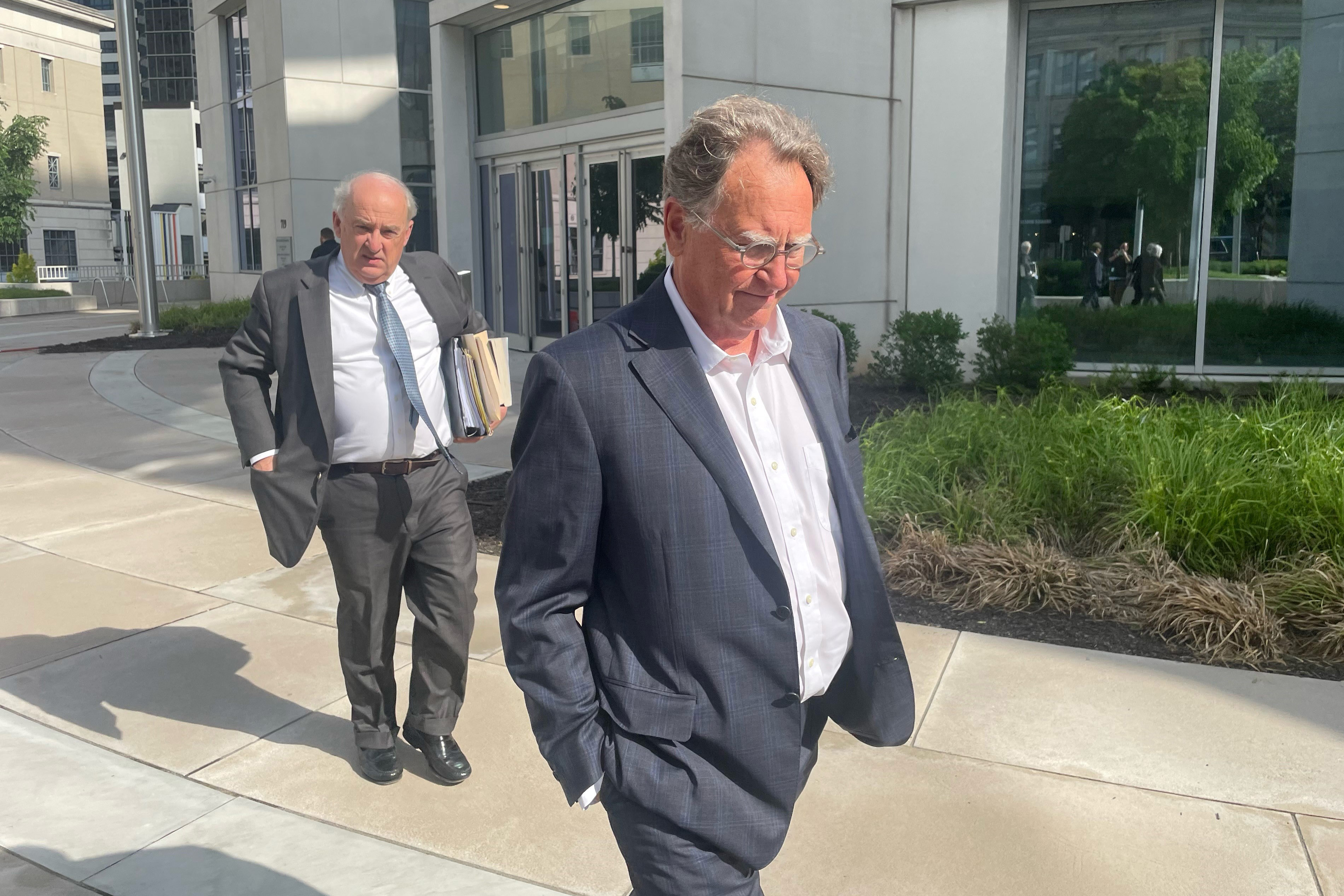 A photo of a man in a suit walking outside a courthouse with another man following behind him.