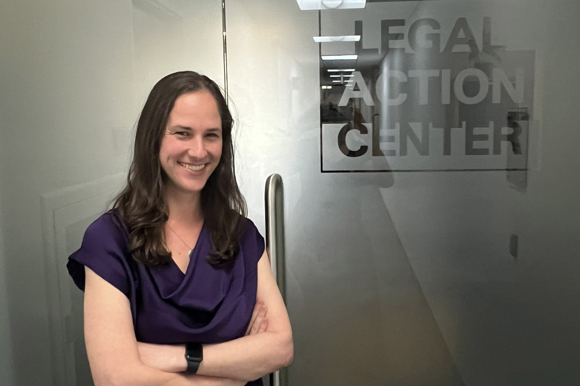 A photo of a woman posing in front of a conference room door with Legal Action Center's logo printed on it.