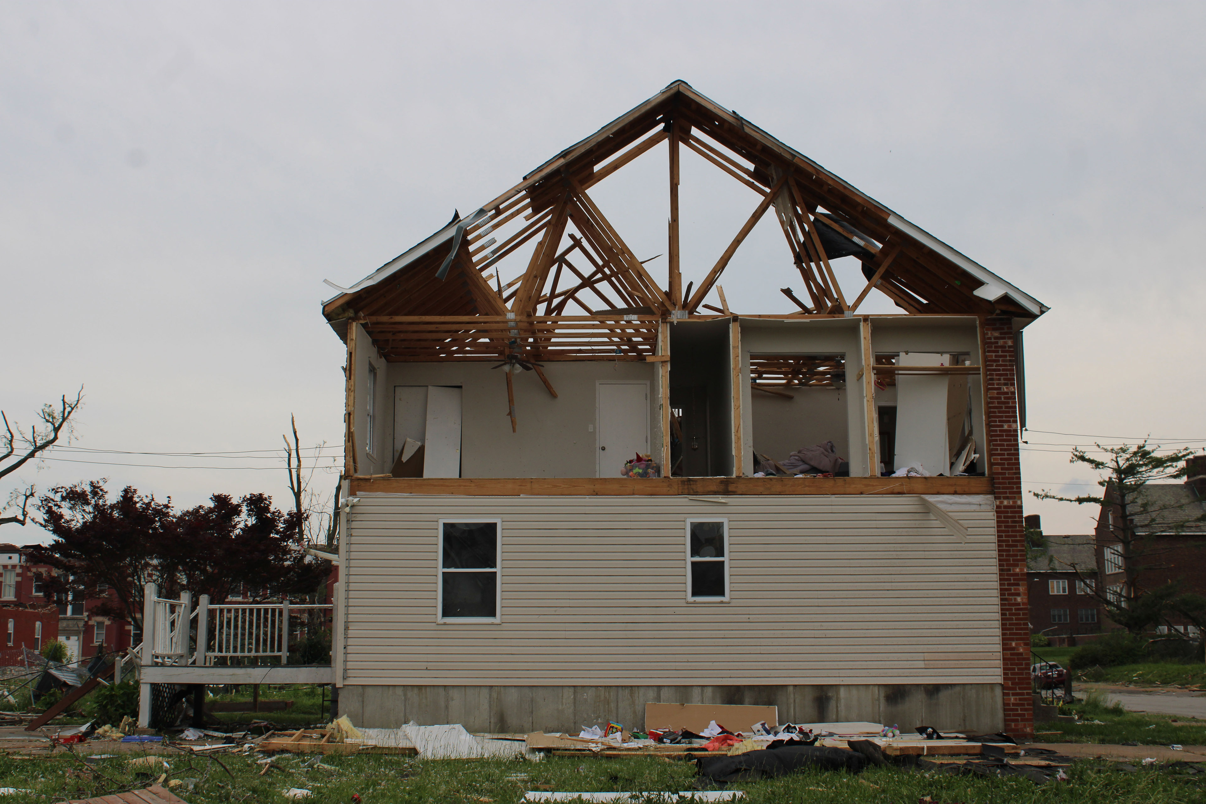A photo of a house severely damaged by a tornado. The upper half's walls have blown away, leaving just the roof frame behind.