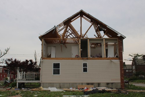 A photo of a house severely damaged by a tornado. The upper half's walls have blown away, leaving just the roof frame behind.