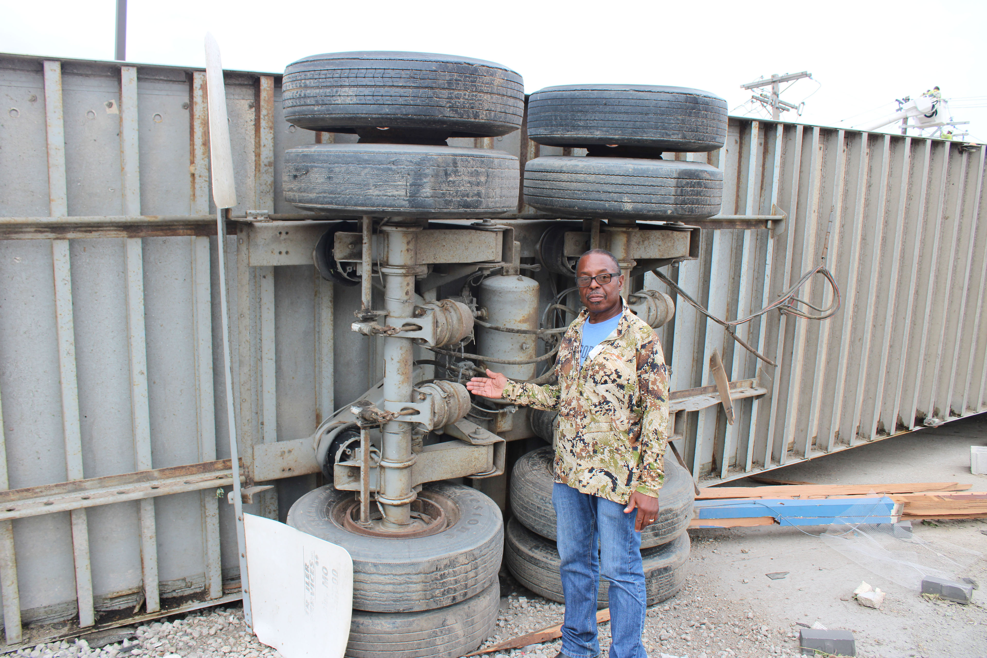 A photo of a man gesturing to an overturned tractor trailer.