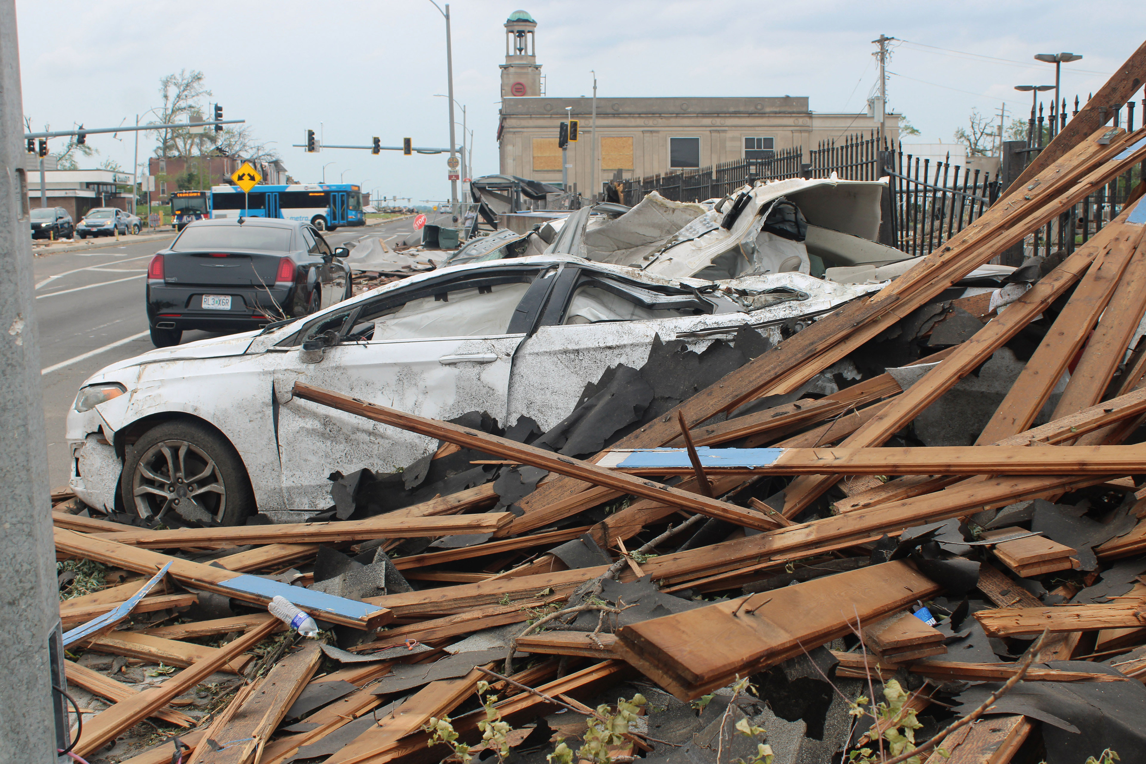 On the side of a road, a car is severely damaged. Slats of wood surround it.