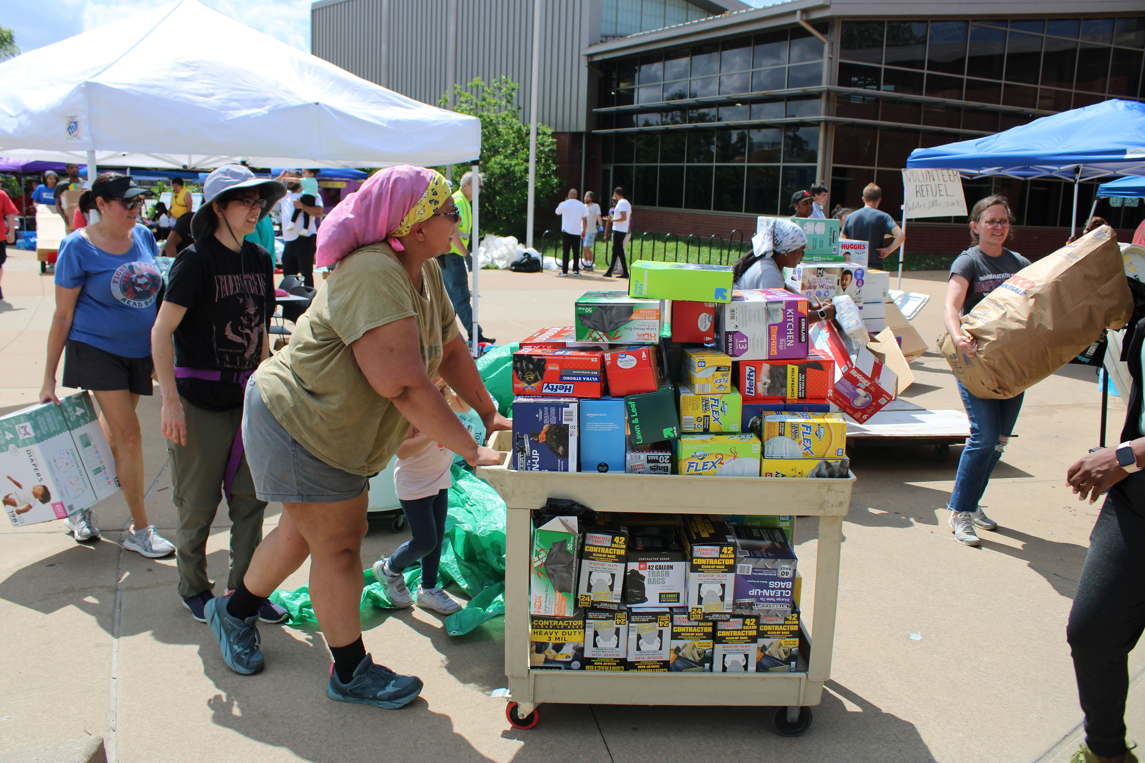 A photo of a woman wheeling in a trolley cart filled with trash bags at a community center.