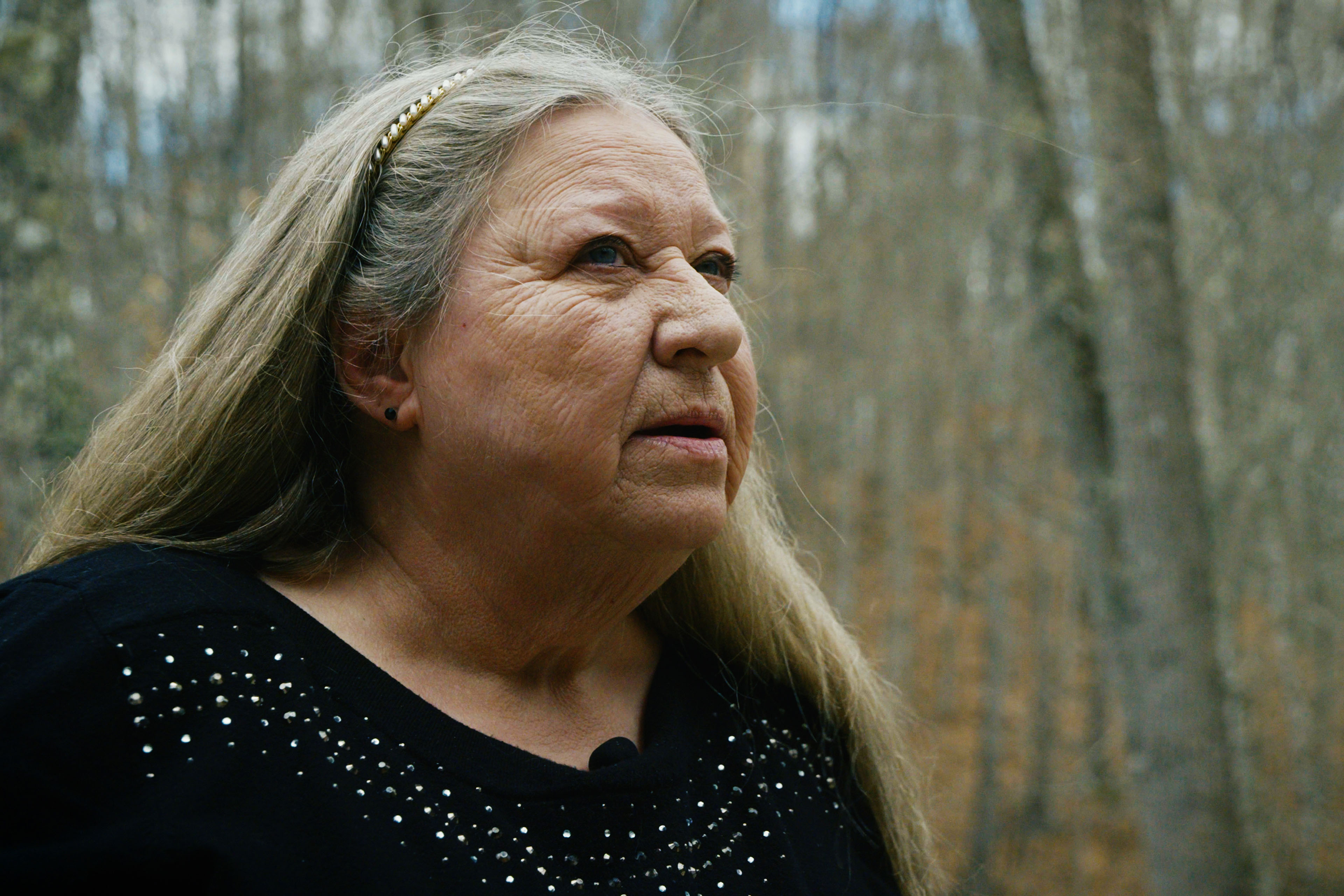A woman wearing a black sweater poses for a portrait among tall trees
