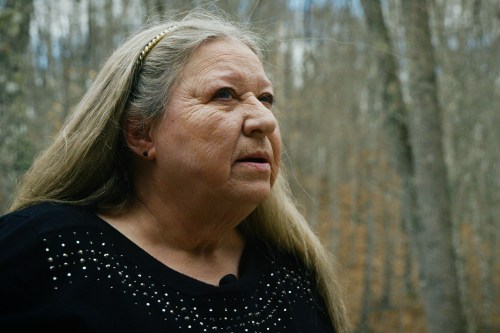 A woman wearing a black sweater poses for a portrait among tall trees
